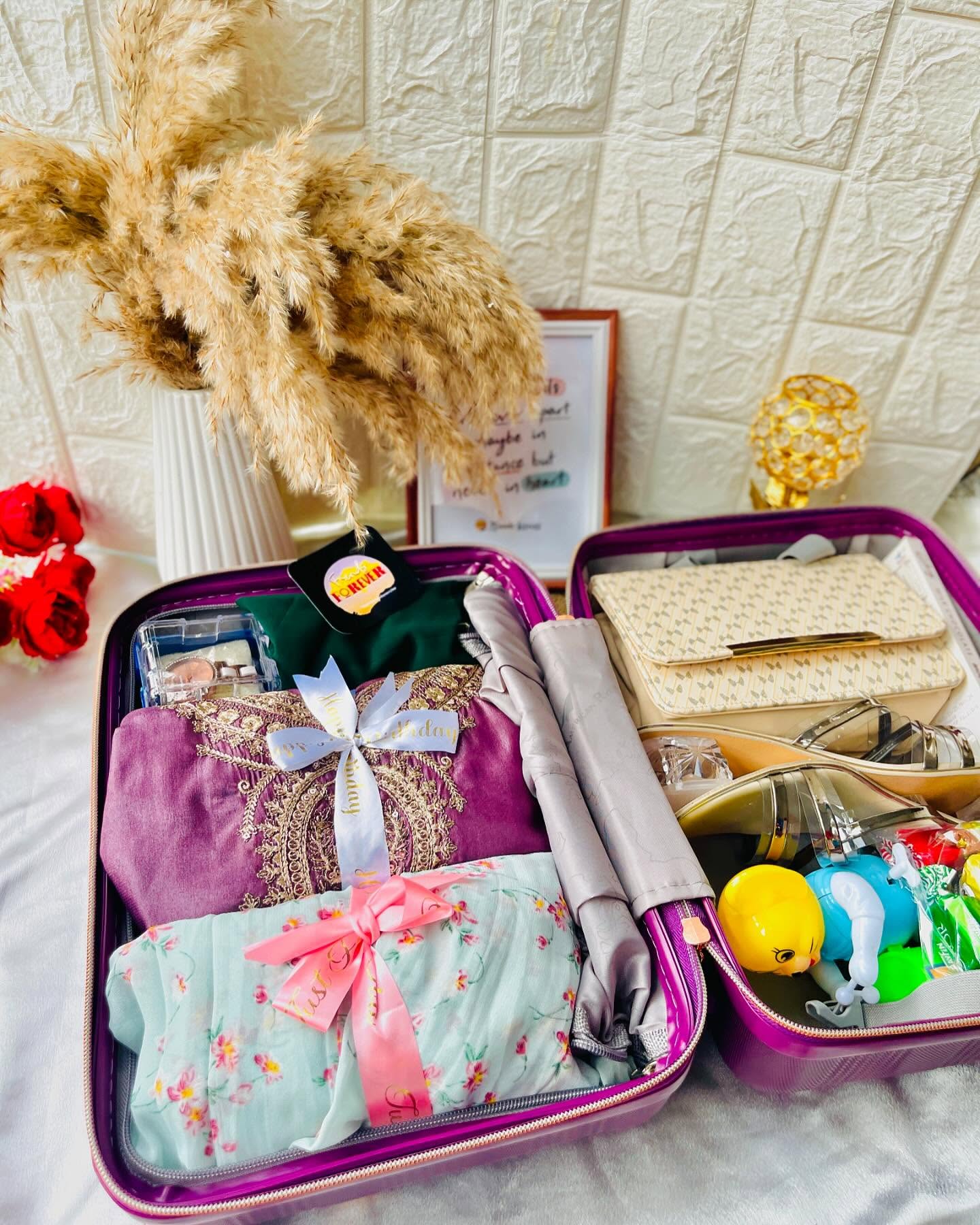 A magenta travel suitcase dressed with a floral wrap and gold "Happy Birthday" topper, paired with a rose and chocolate bouquet.