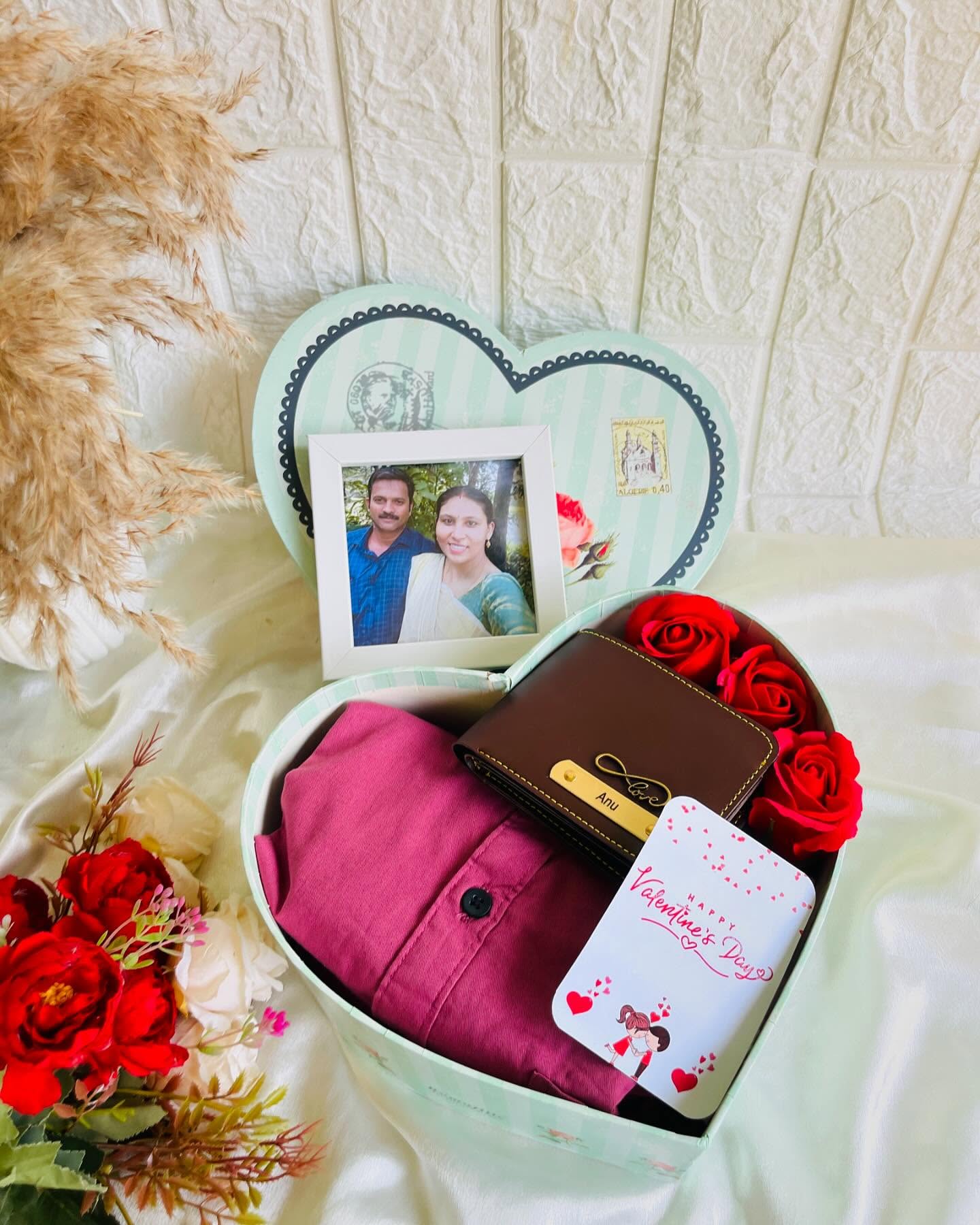 A heart-shaped gift box with a personalized leather wallet, a framed couple photo, red roses and a Valentine's card.
