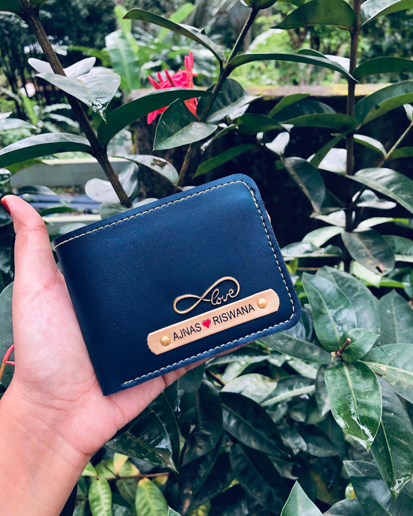 A navy leather wallet stamped with an infinity love symbol and the couple's names on a tan nameplate.