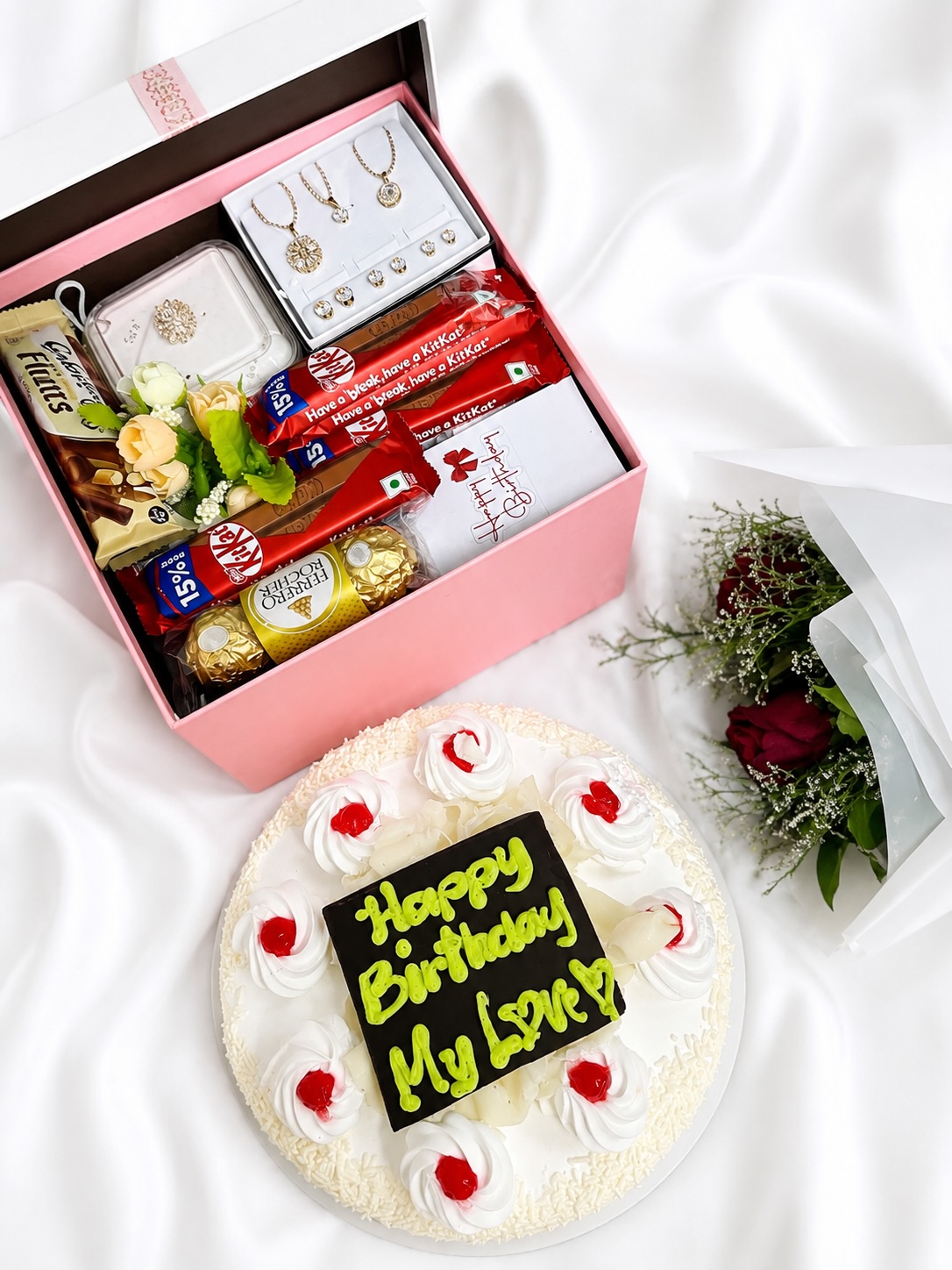 A pink birthday hamper loaded with jewellery, Ferrero Rocher, KitKat and Cadbury chocolates, paired with a fresh rose bouquet and a personalised cake.