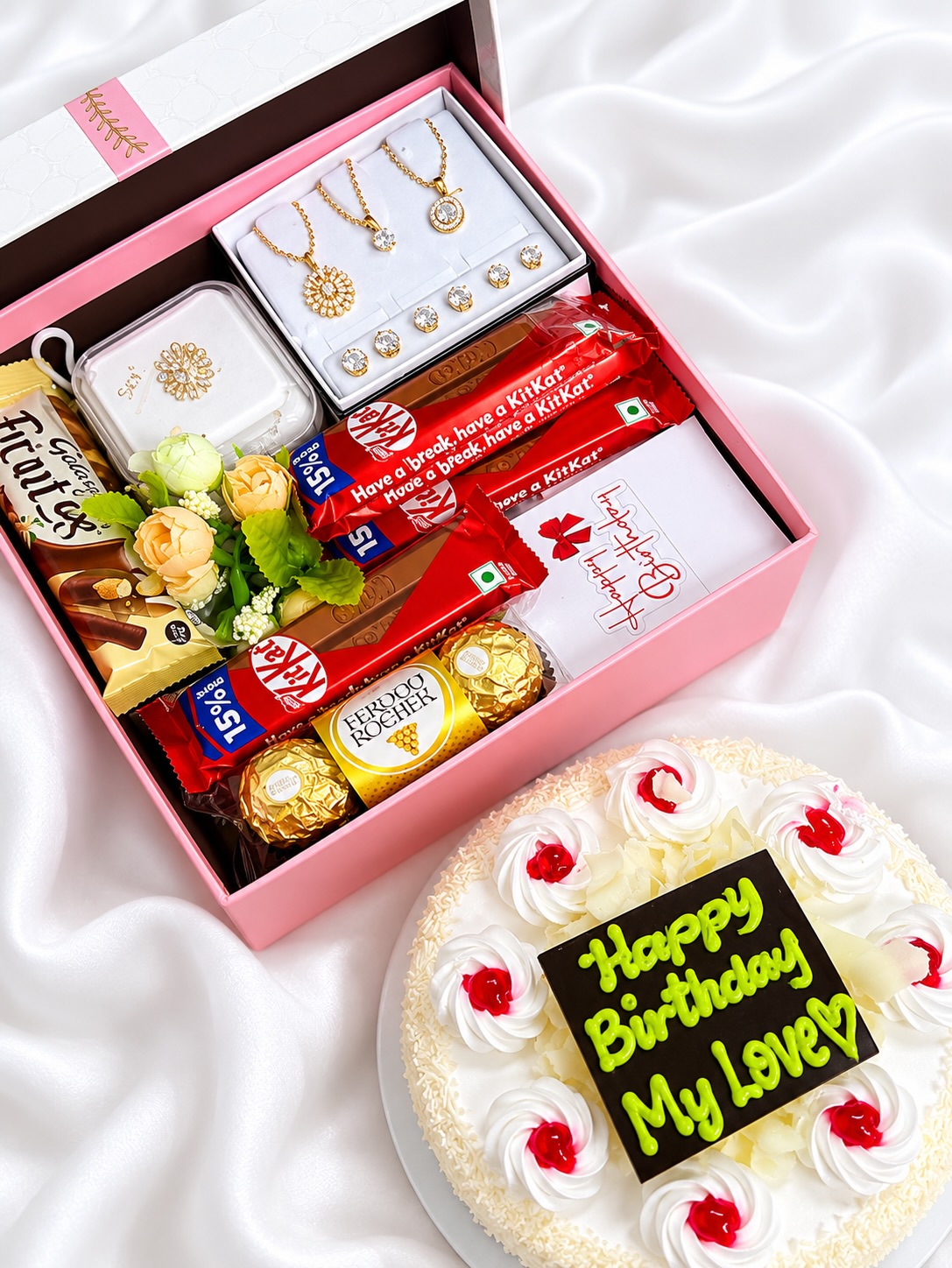 An elegant pink gift box pairing a sparkling jewelry set with Ferrero Rocher, KitKat bars and fresh flowers, finished with a matching celebration cake.