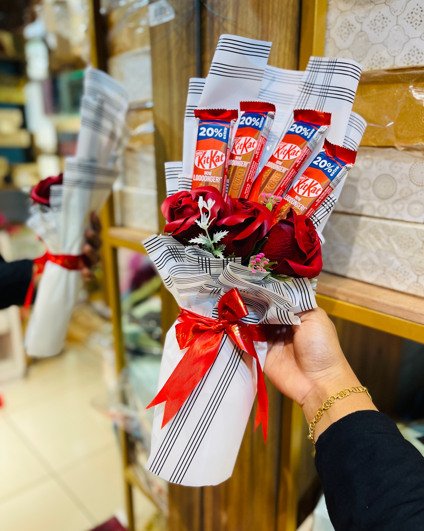 A hand-tied bouquet pairing velvet red roses with KitKat chocolate bars, wrapped in patterned paper with a red satin bow.