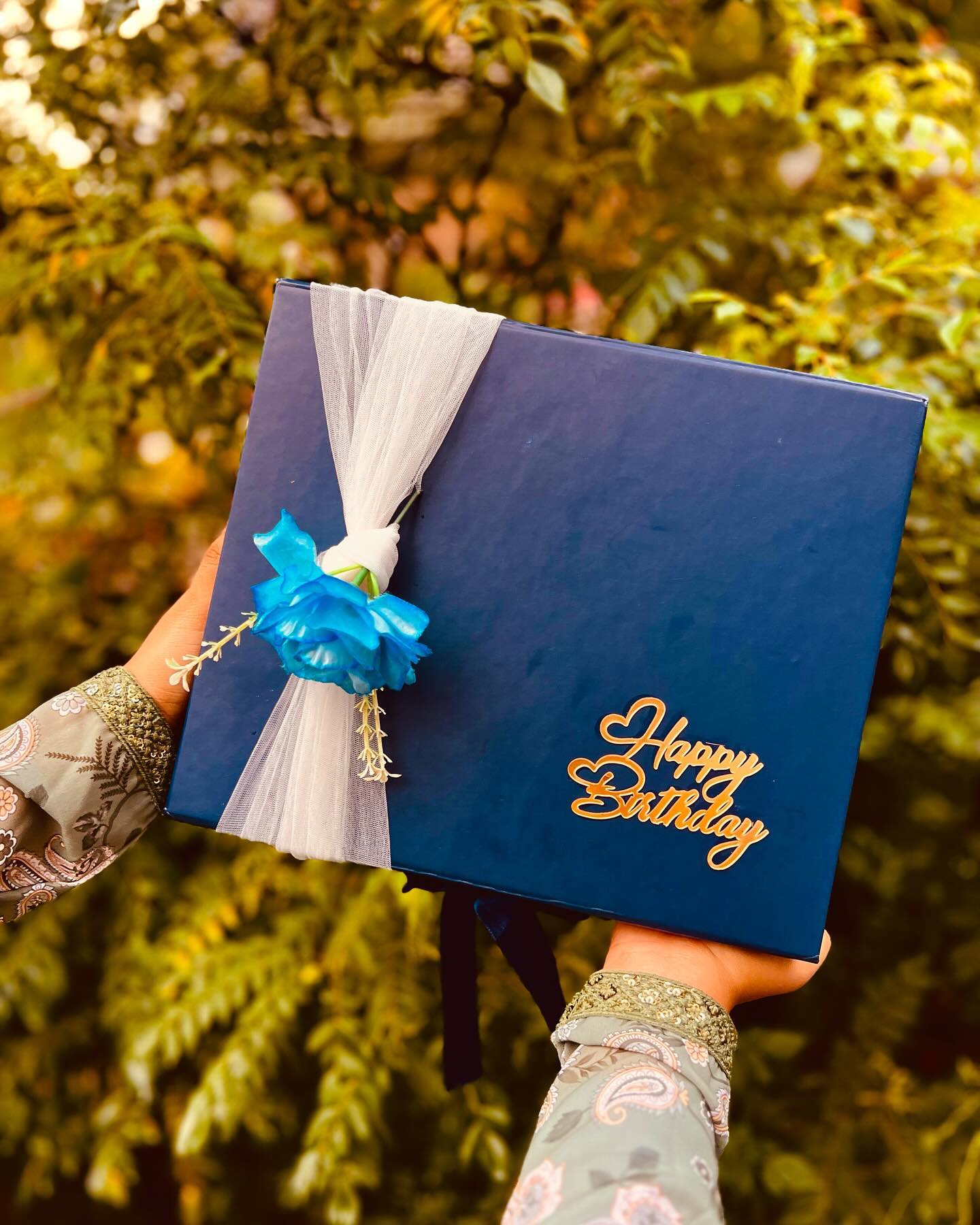 A navy gift box layered with KitKats, white roses, a couple photo frame, and elegant drop earrings.