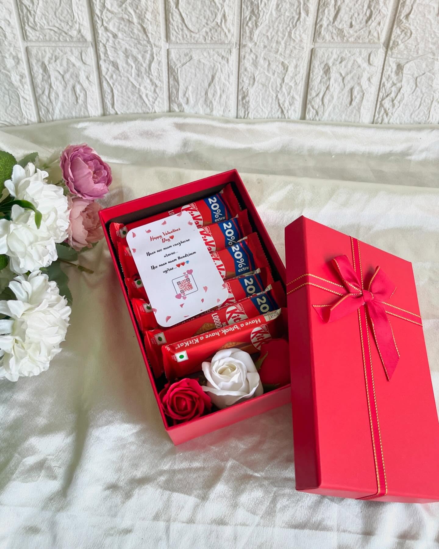 A ruby-red gift box lined with KitKats and a personalized Valentine's message card, topped with a satin bow.