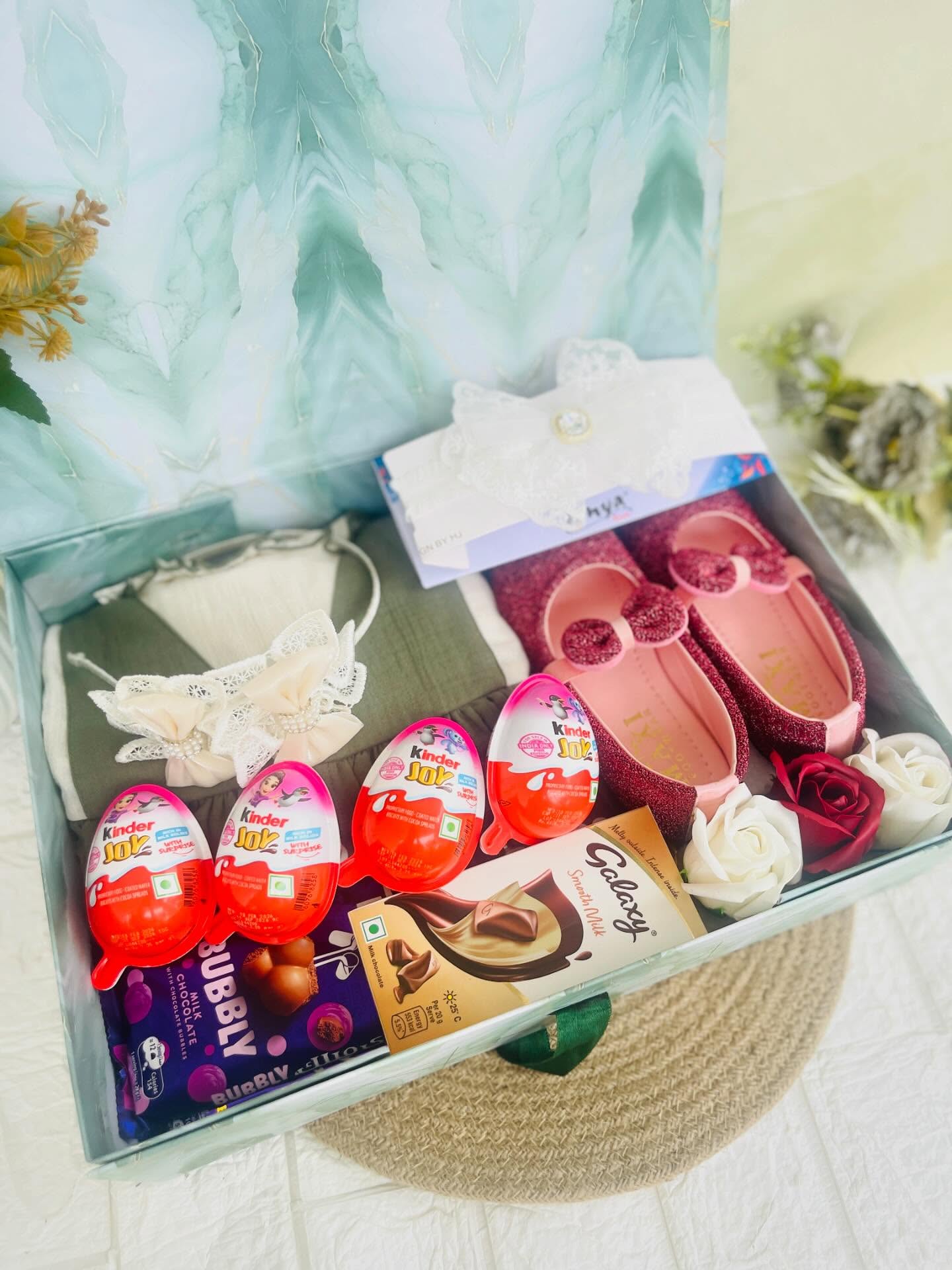 A mint gift box filled with glittery baby shoes, a lace headband, Kinder Joy eggs and chocolates for a special little girl.
