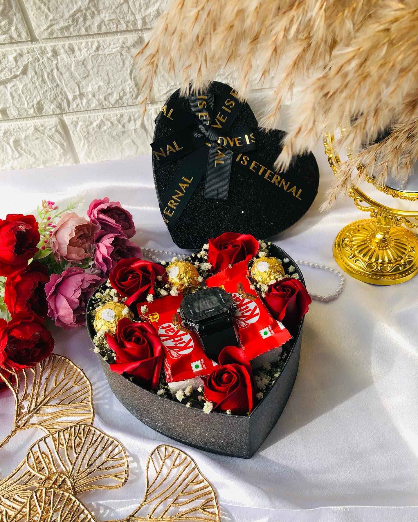 A black heart-shaped box filled with red roses, Ferrero Rocher, KitKat bars, and a black Casio watch for him.