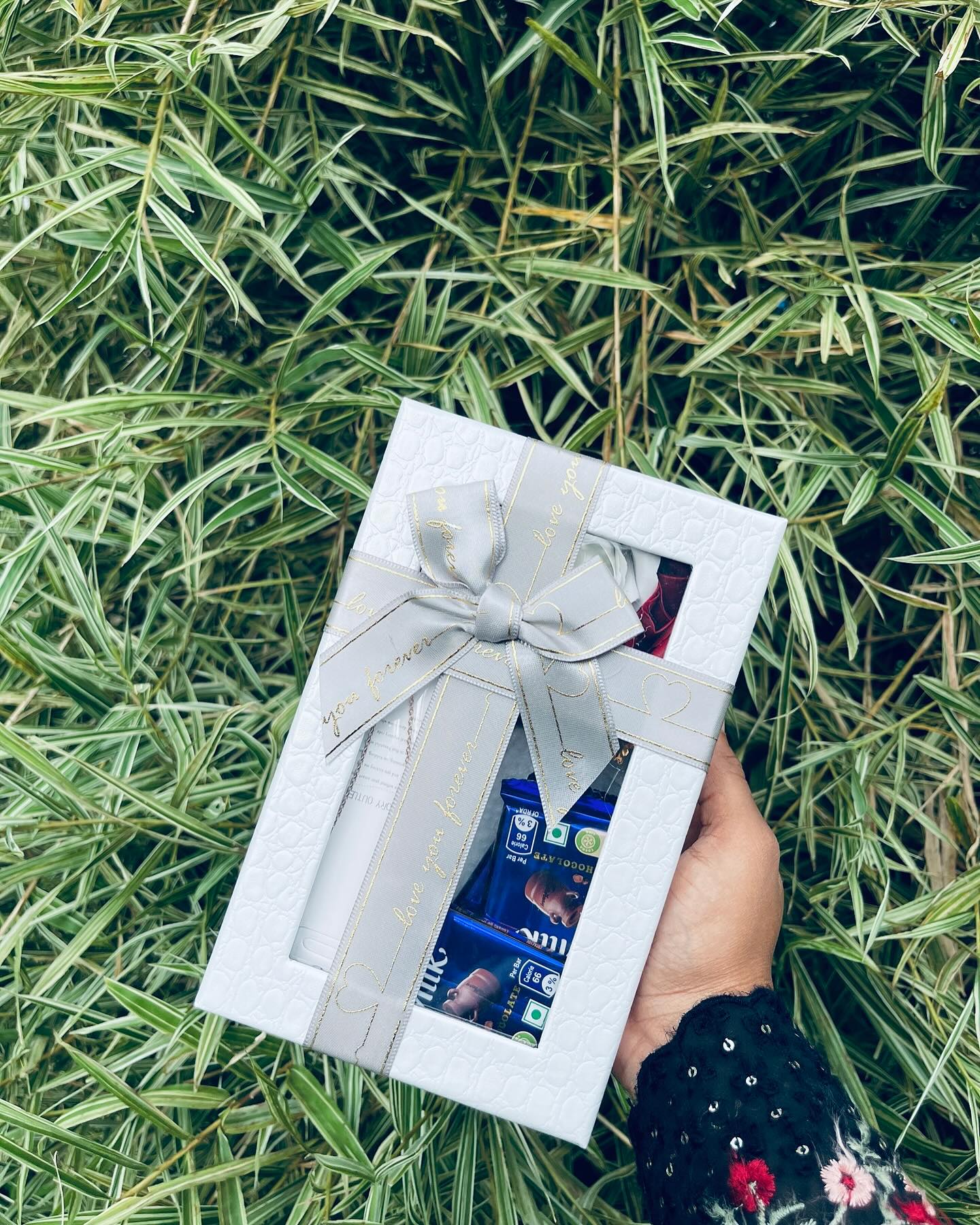 A textured white gift box tied with a 'love you forever' ribbon, filled with chocolate bars for a sweet romantic gesture.