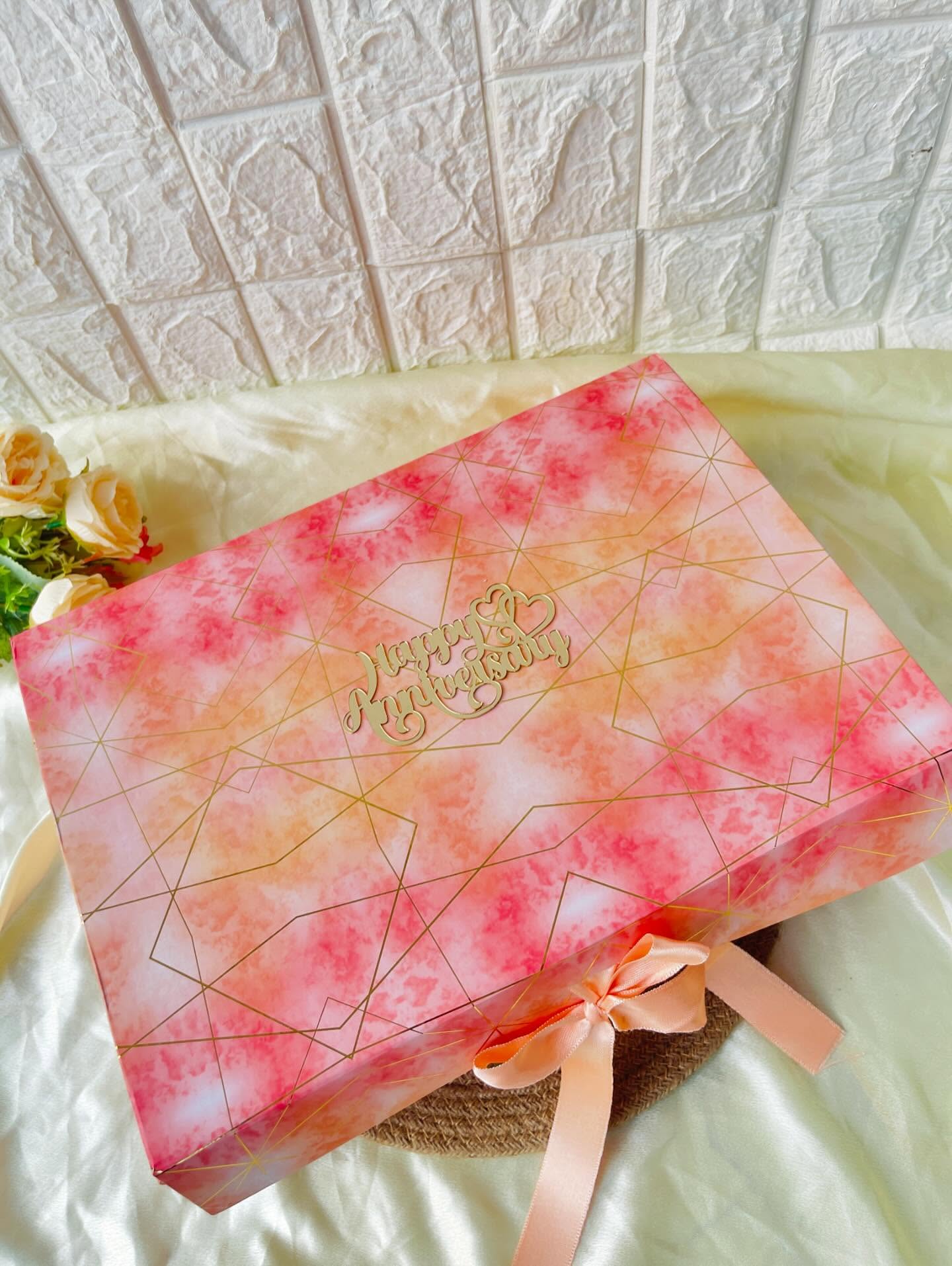 A rose-gold marbled gift box topped with a laser-cut 'Happy Anniversary' script and satin ribbon.