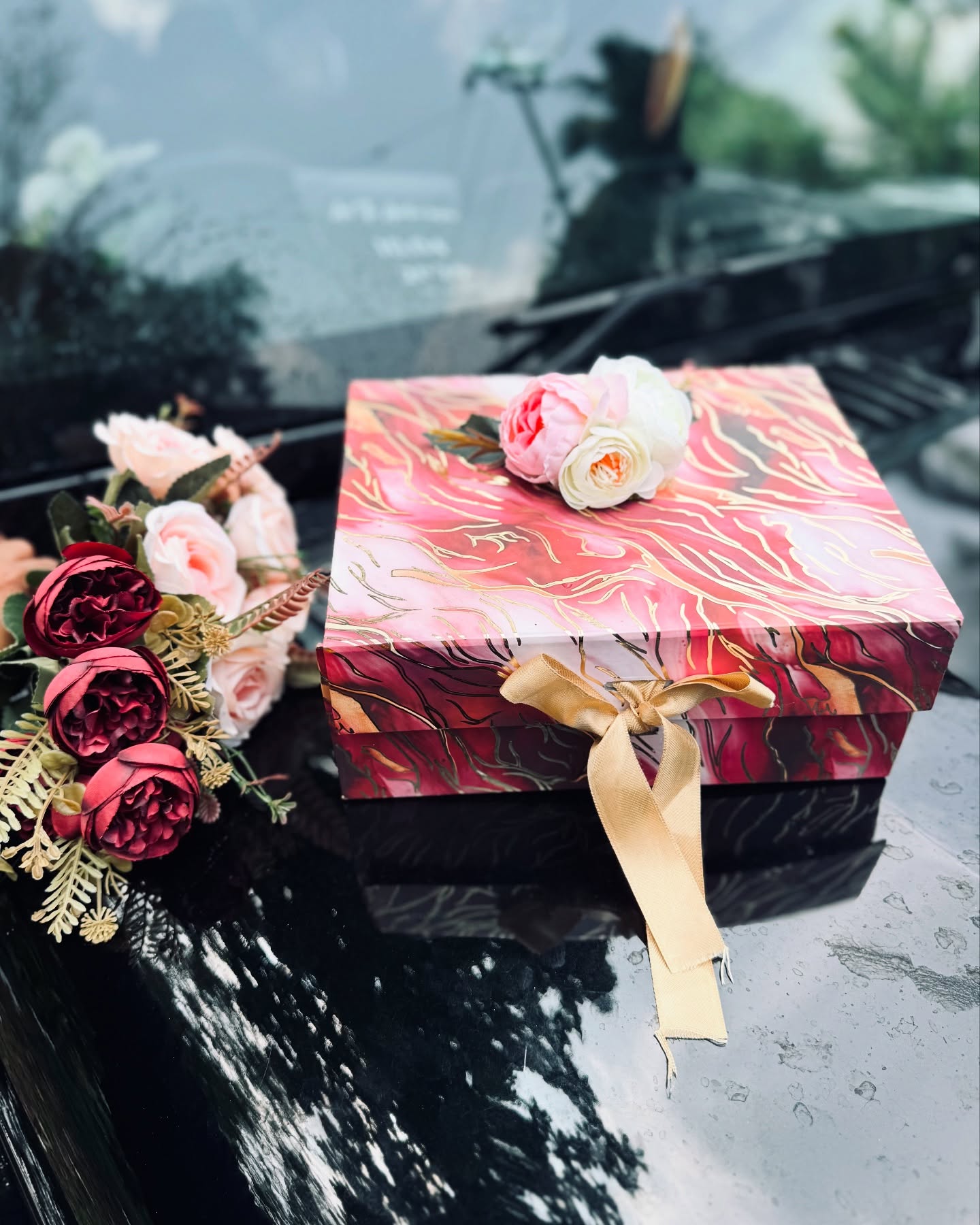 A hand-painted red and gold marble-effect gift box topped with soft pink and white roses.