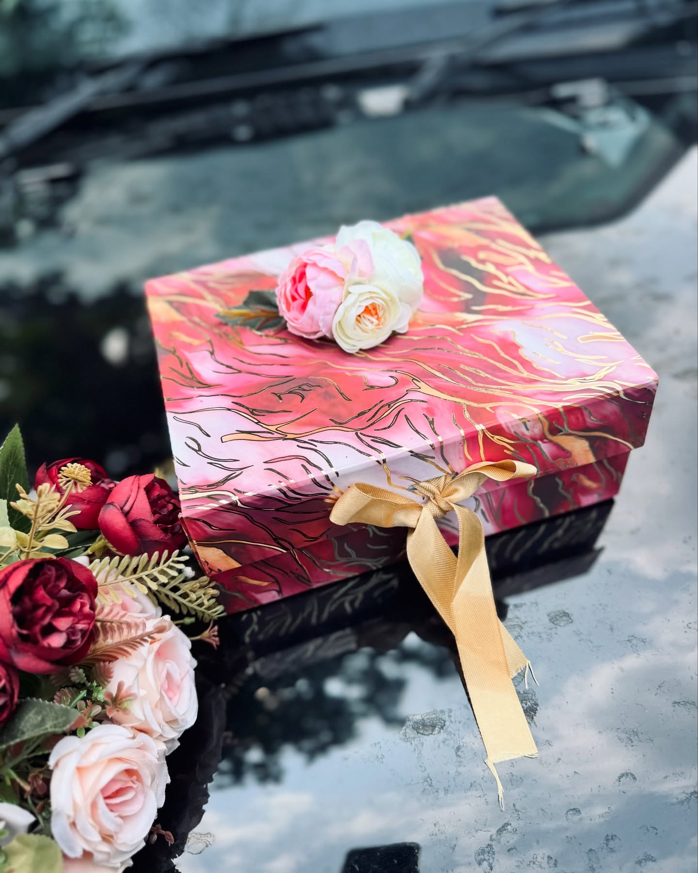 A closed marble-pattern gift box in pink and gold, topped with a delicate rose duo and satin ribbon.