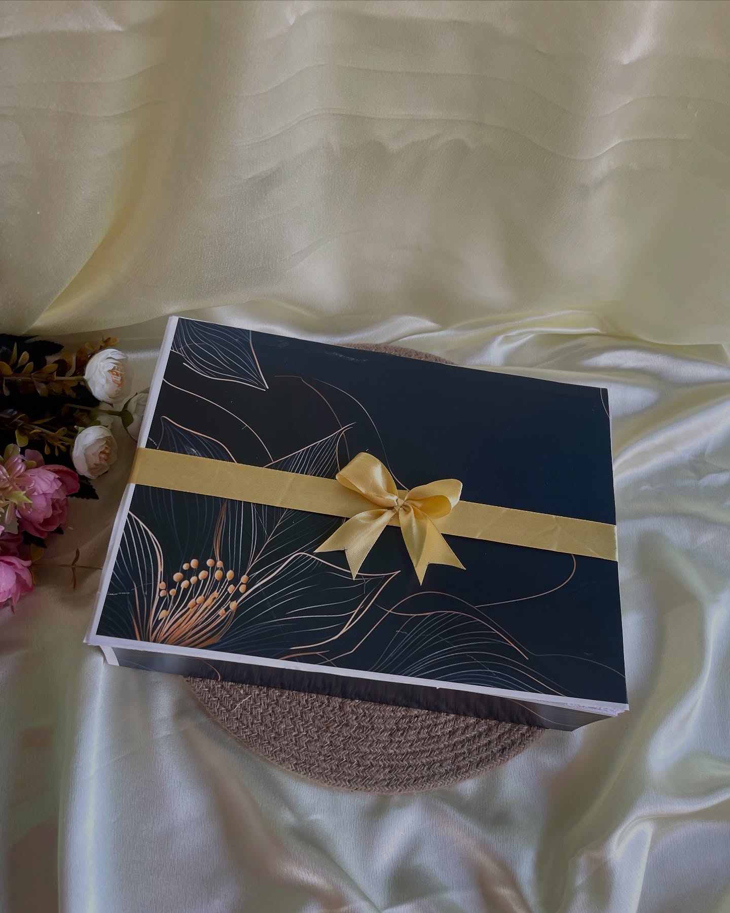 An elegant black gift box with a gold botanical print, cinched with a satin gold bow.