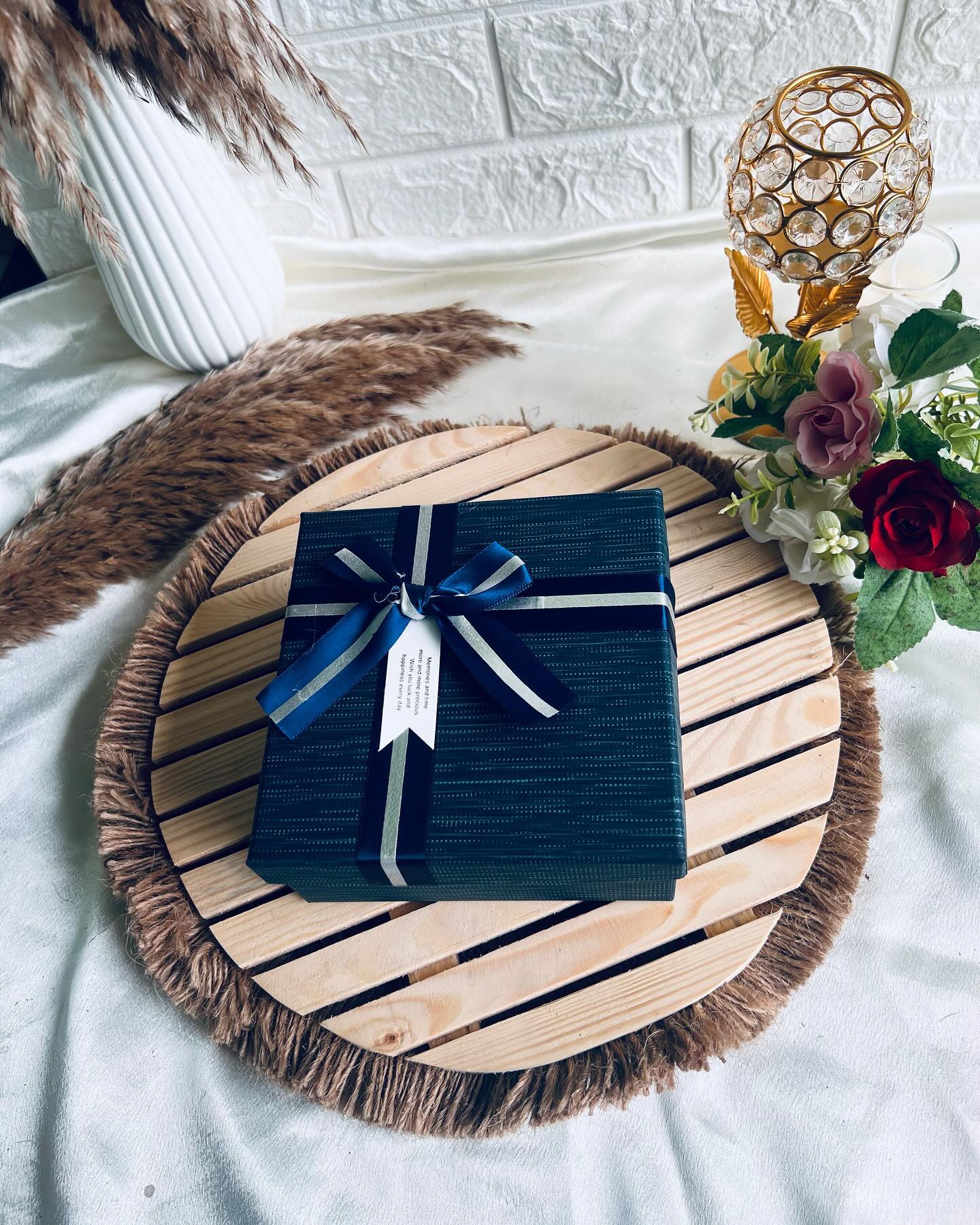 A deep navy gift box wrapped with a satin-and-silver ribbon and a heartfelt memories and time message tag.