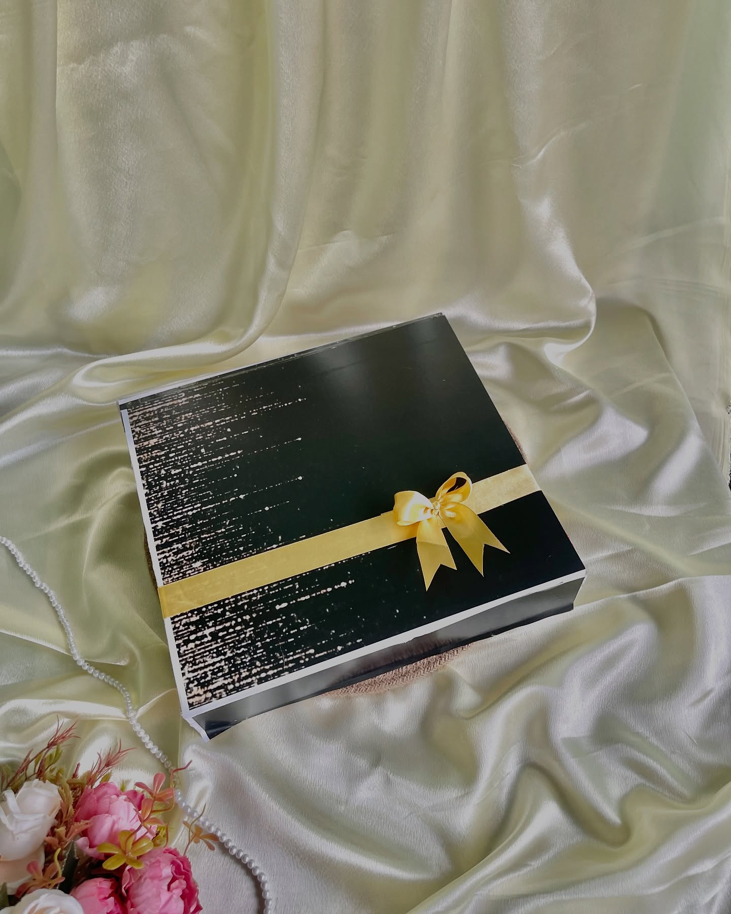 A sleek black gift box wrapped with a golden satin ribbon and bow, ready for any celebration.