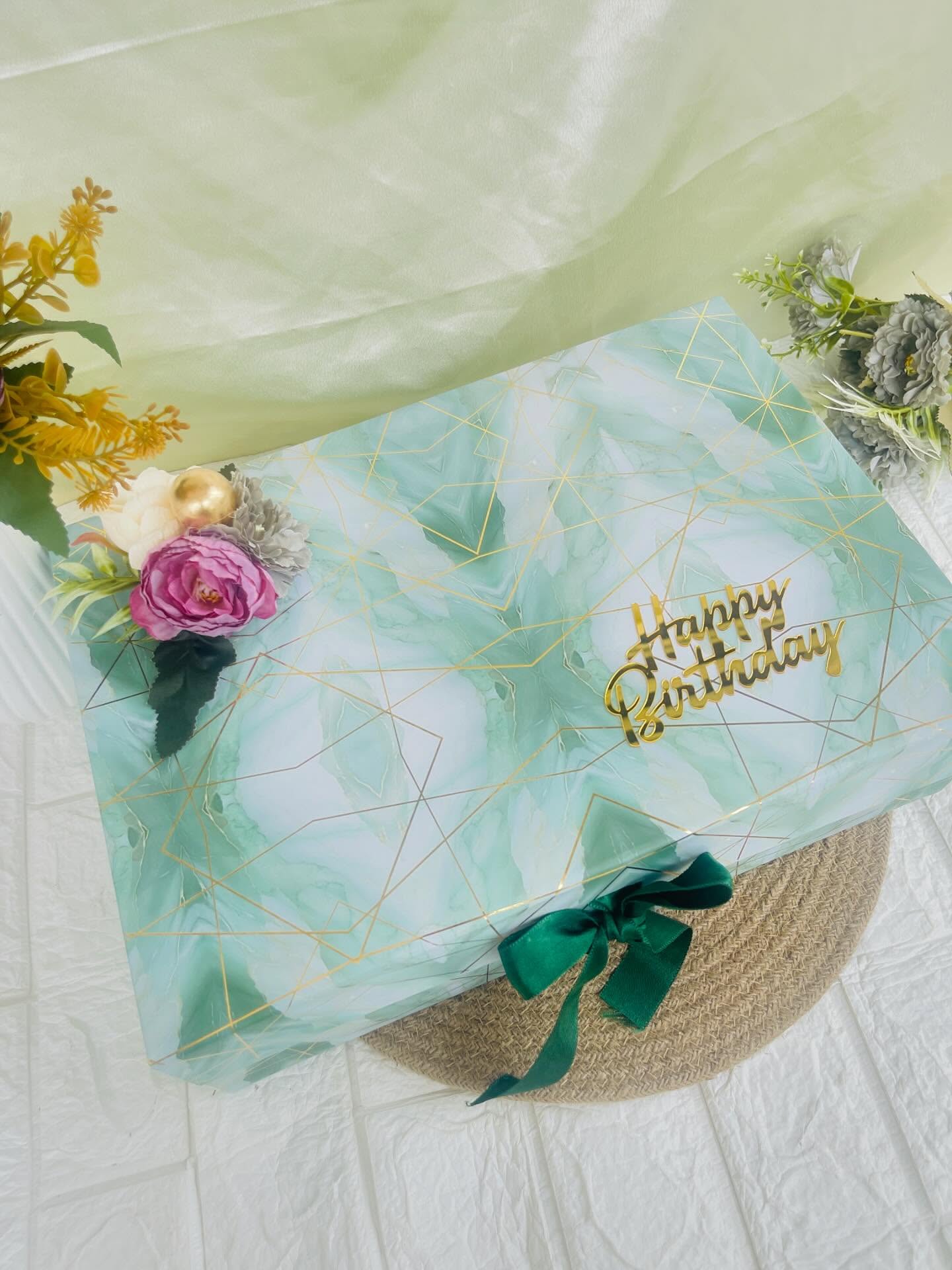 An elegant mint-and-gold marble gift box finished with fresh florals and a forest-green ribbon for a birthday surprise.