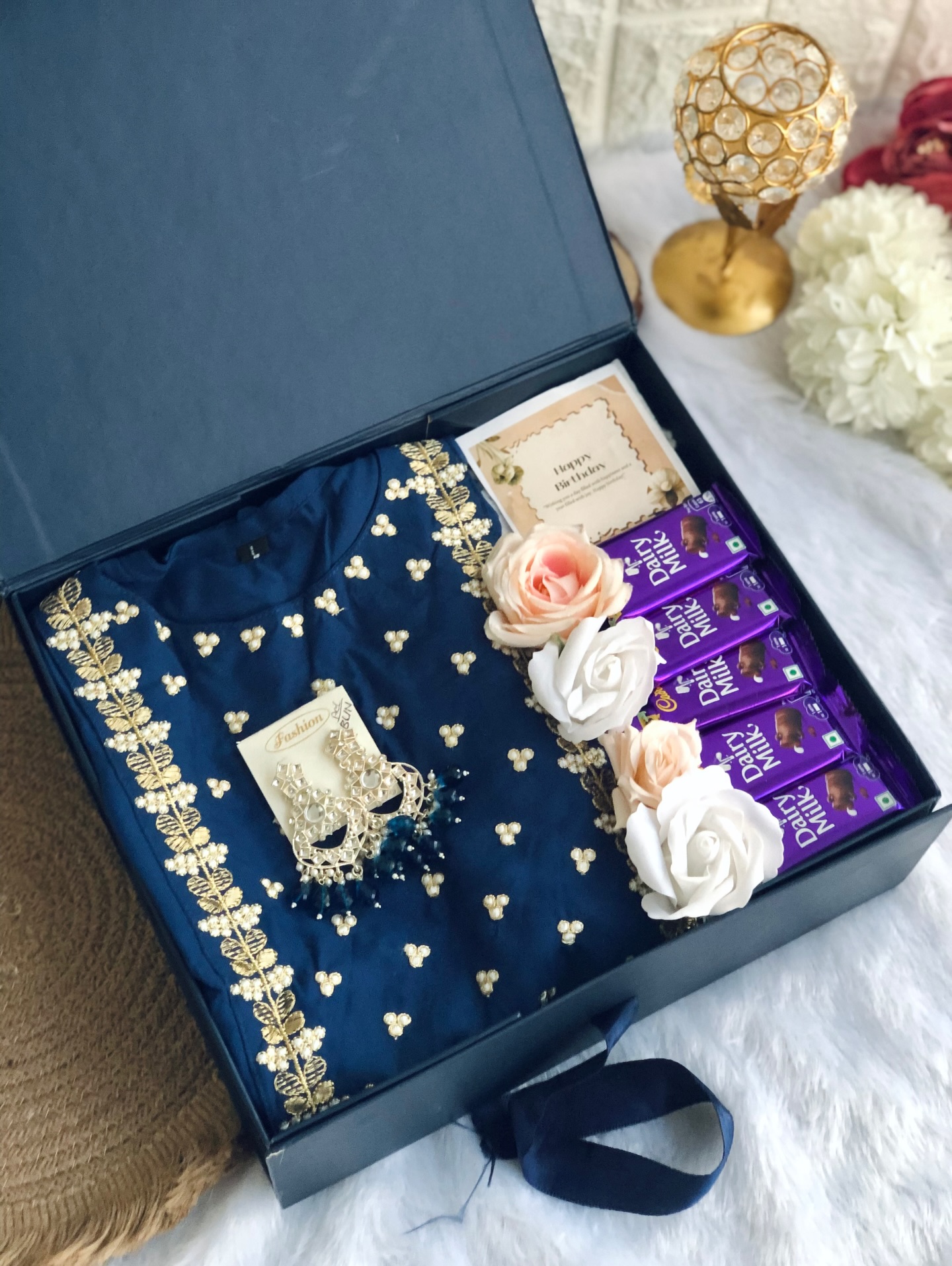 A birthday gift box with a pearl-embroidered navy kurti, statement jhumka earrings, Dairy Milk chocolates, and roses.