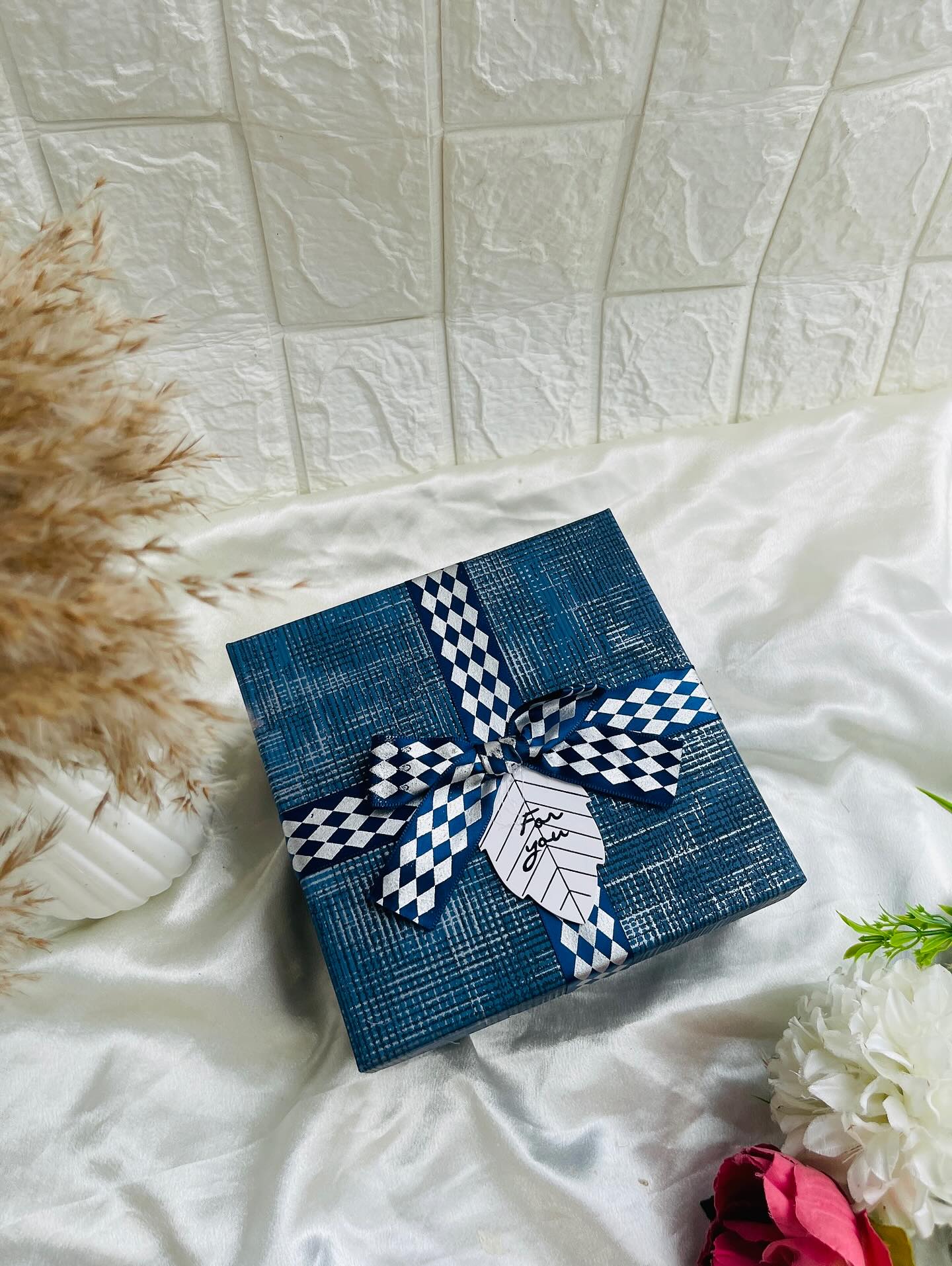 An elegantly wrapped navy textured gift box finished with a checkered ribbon bow and a 'For You' tag.