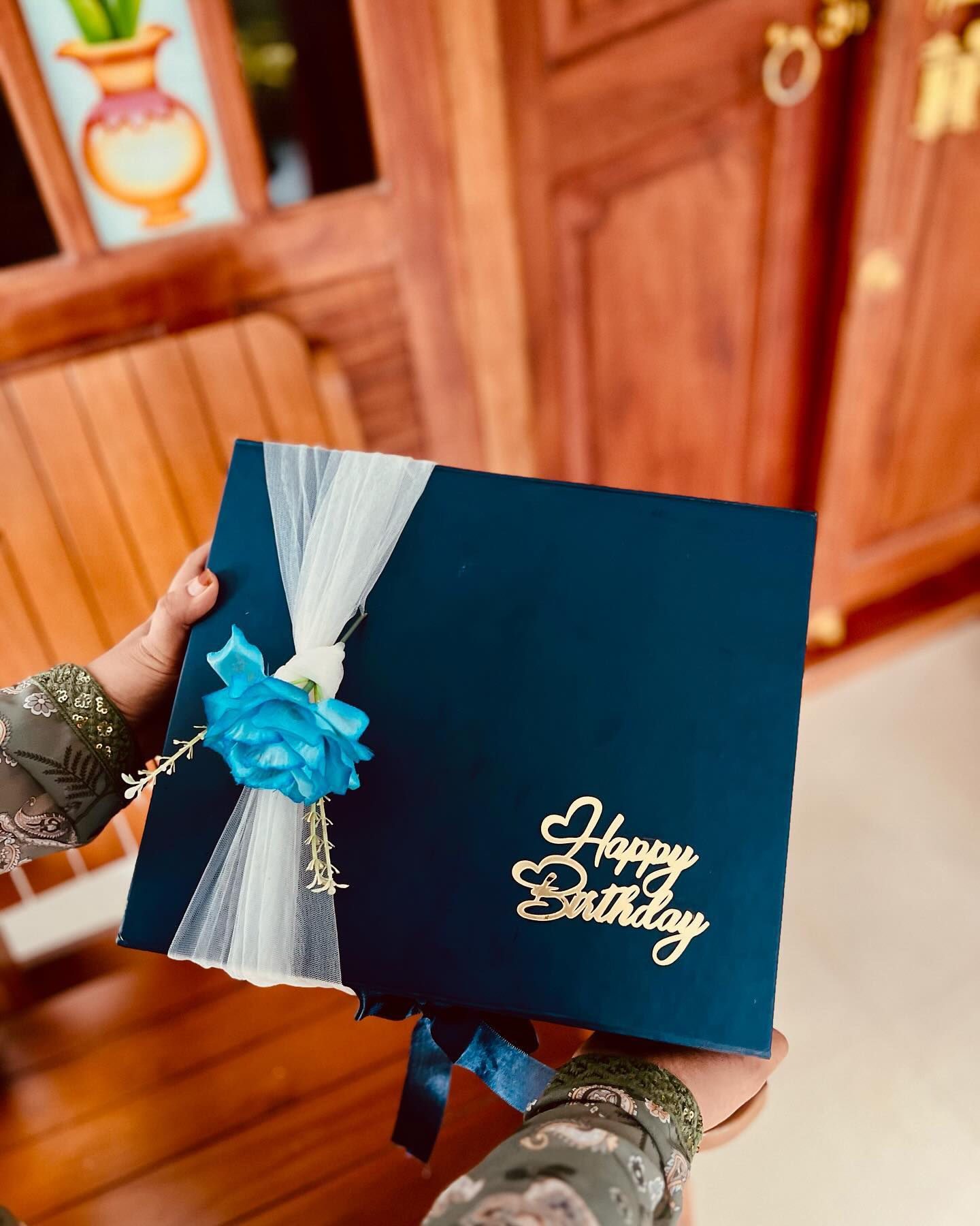 An elegant navy gift box wrapped in tulle with a teal rose accent and a gold Happy Birthday topper.