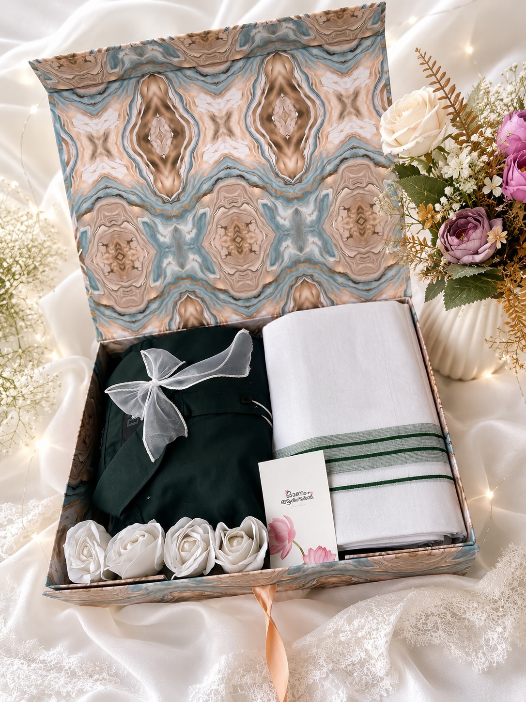 A festive Onam gift box with a traditional white mundu, a green shirt, soap roses, and a greeting card.