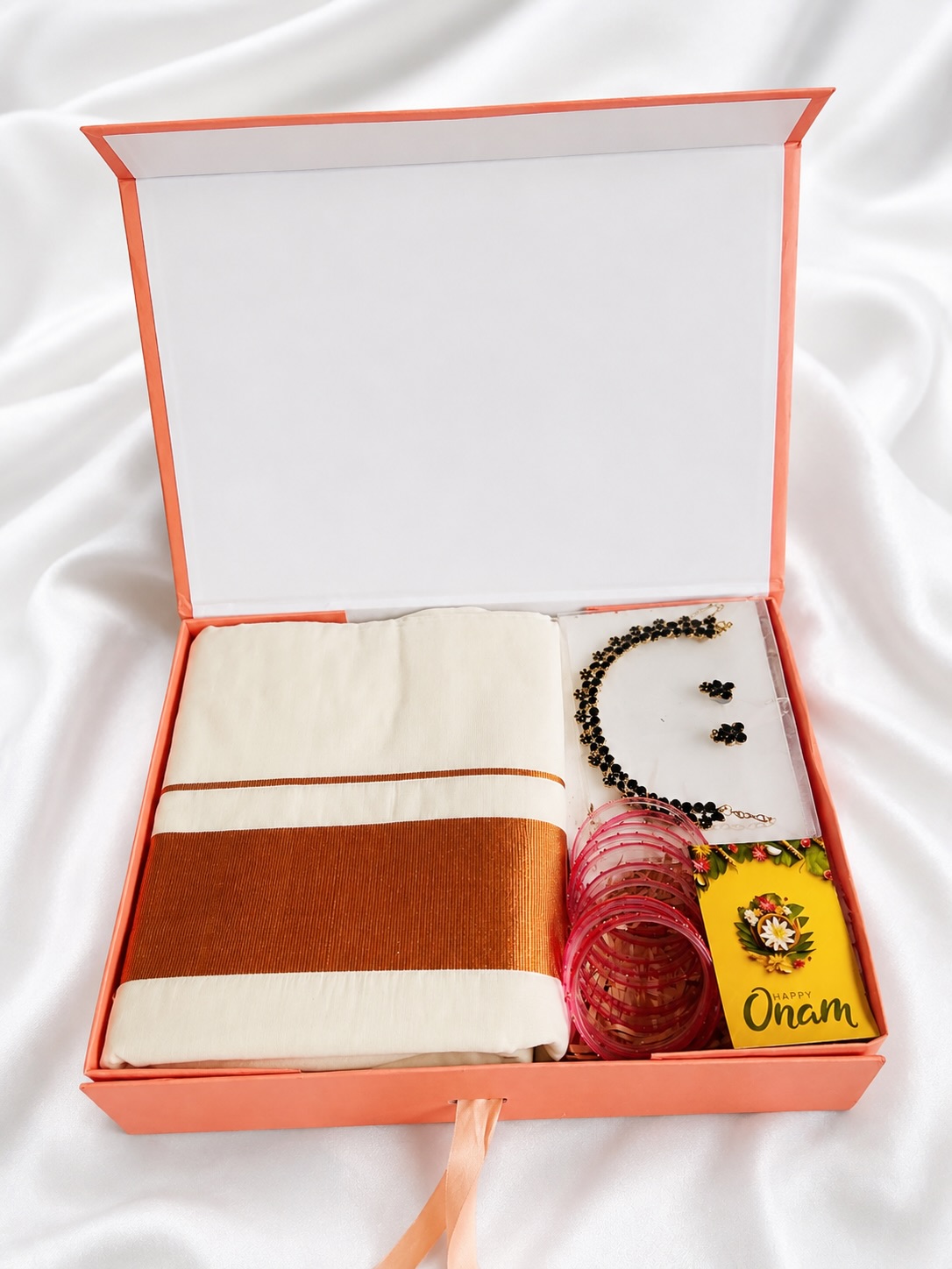 A festive Onam hamper with an off-white and gold-bordered saree, statement jewellery, and pink bangles.