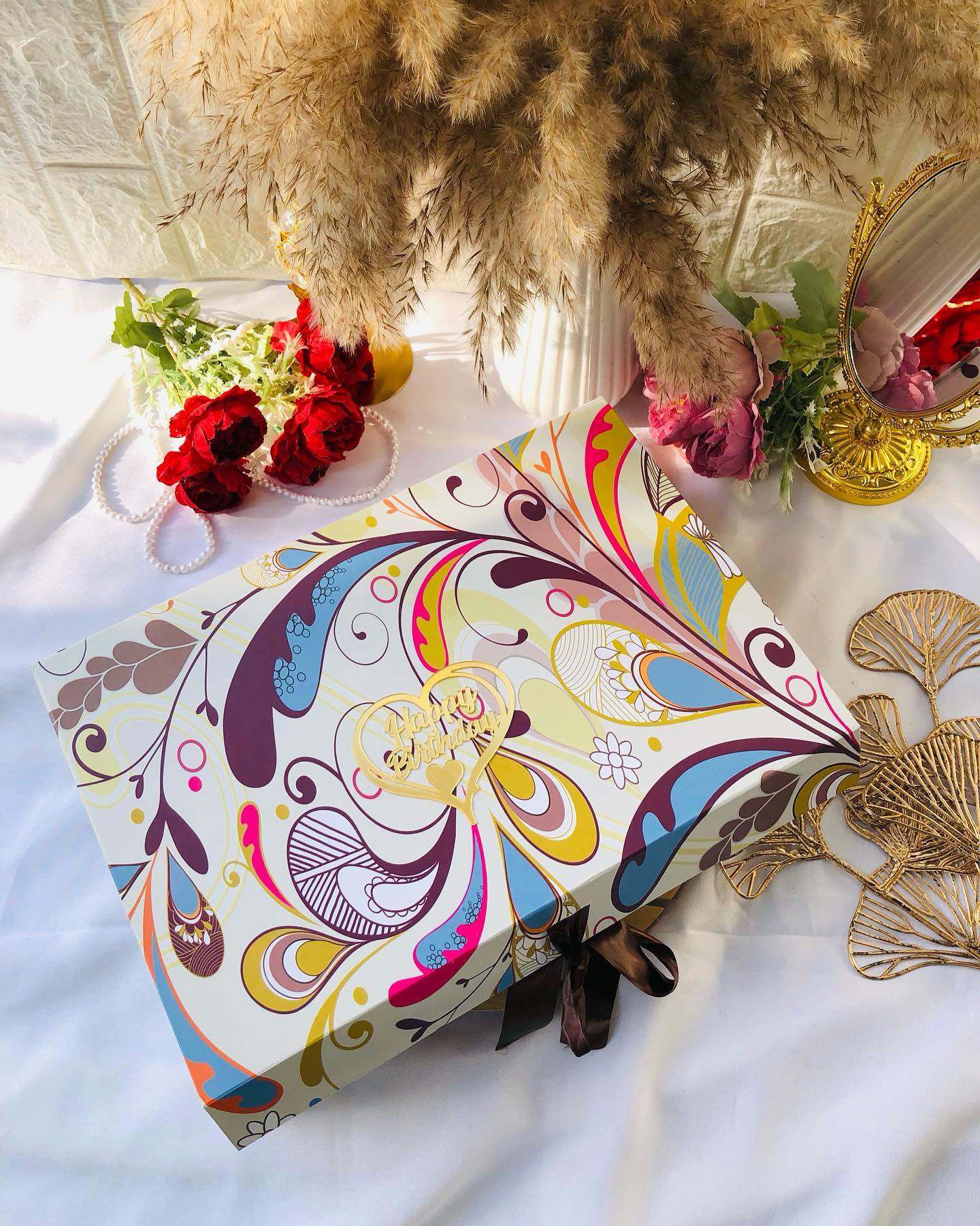 A vividly patterned gift box with a gold "Happy Birthday" heart charm and satin ribbon.
