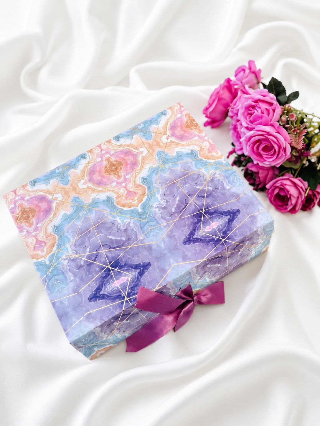 A dreamy pastel agate-marble gift box tied with a plum ribbon bow, paired with a bouquet of pink roses.