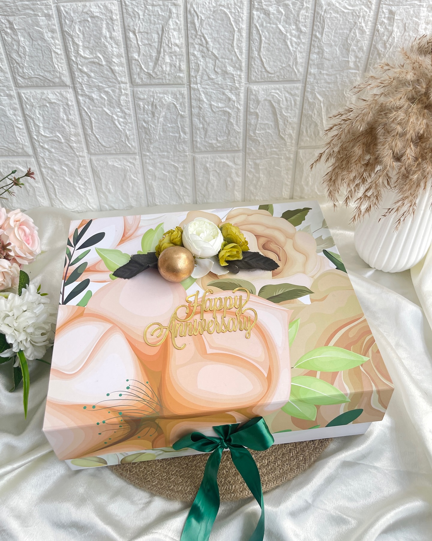 An elegant floral-printed gift box topped with a gold 'Happy Anniversary' script and ribbon.