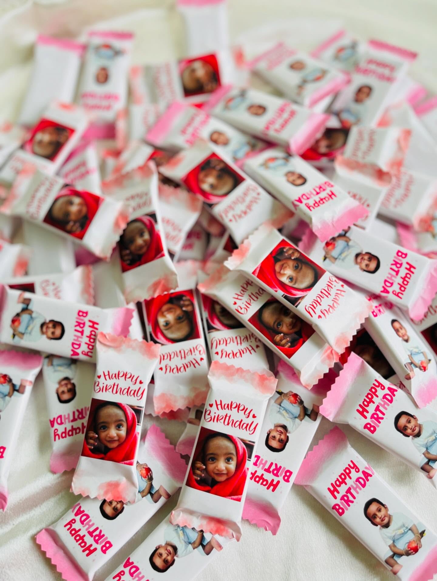 Mini chocolate bars individually wrapped with a baby's photo and 'Happy Birthday' text in soft pink packaging.