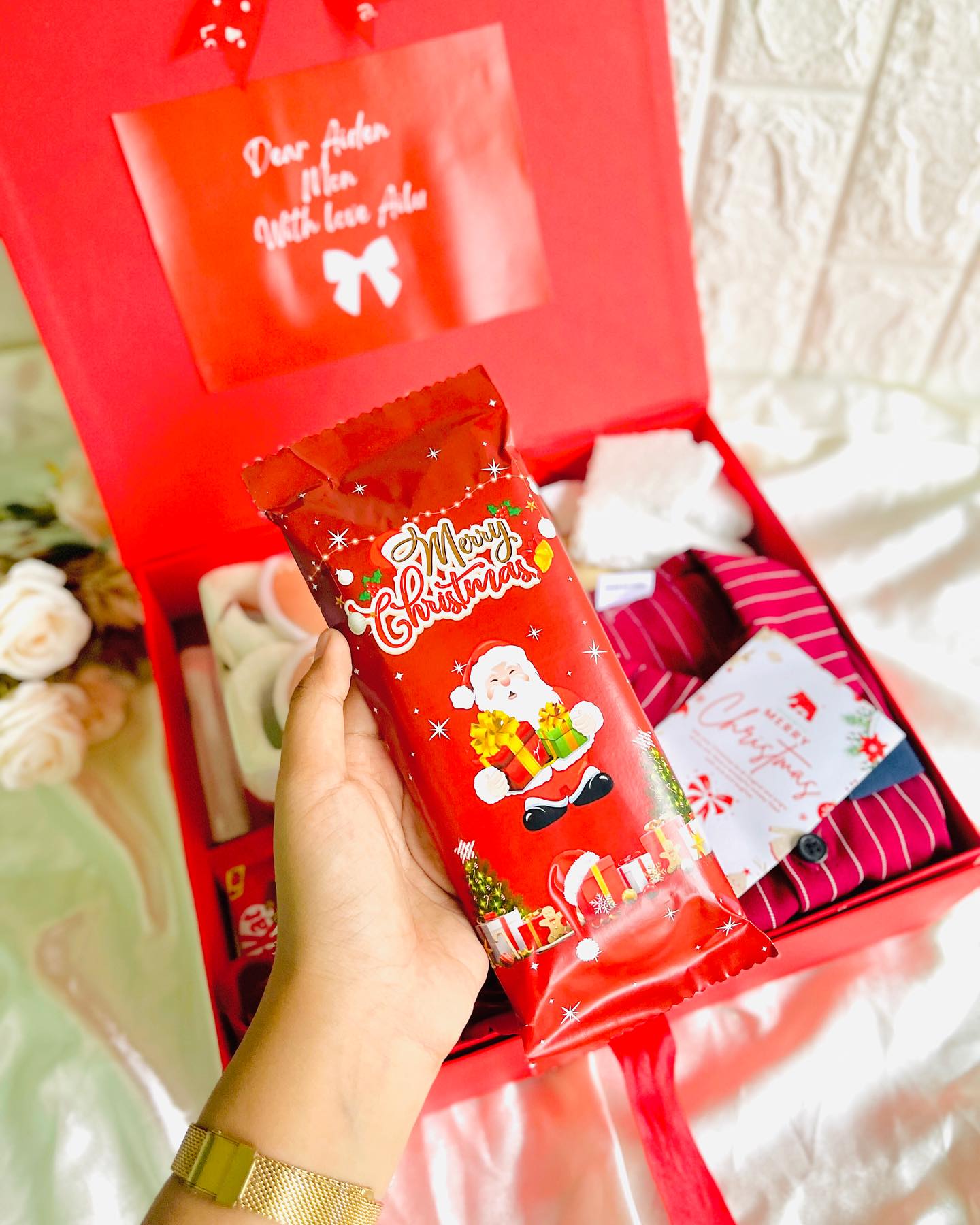 A red gift box with a personalized note, festive treats, and cozy striped loungewear inside.