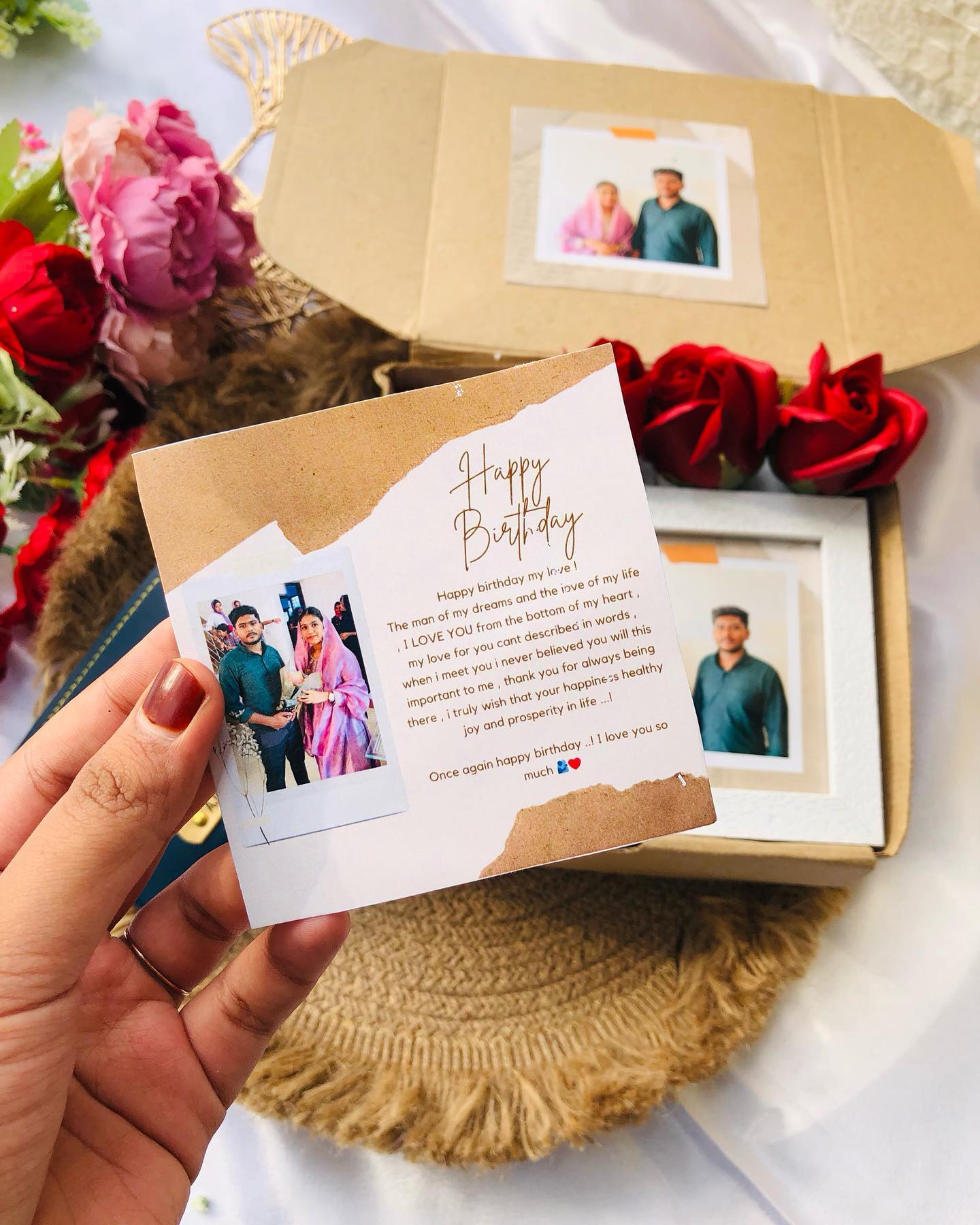 A navy leather wallet engraved with both partners' names and an infinity love symbol, gifted with a couple photo and roses.