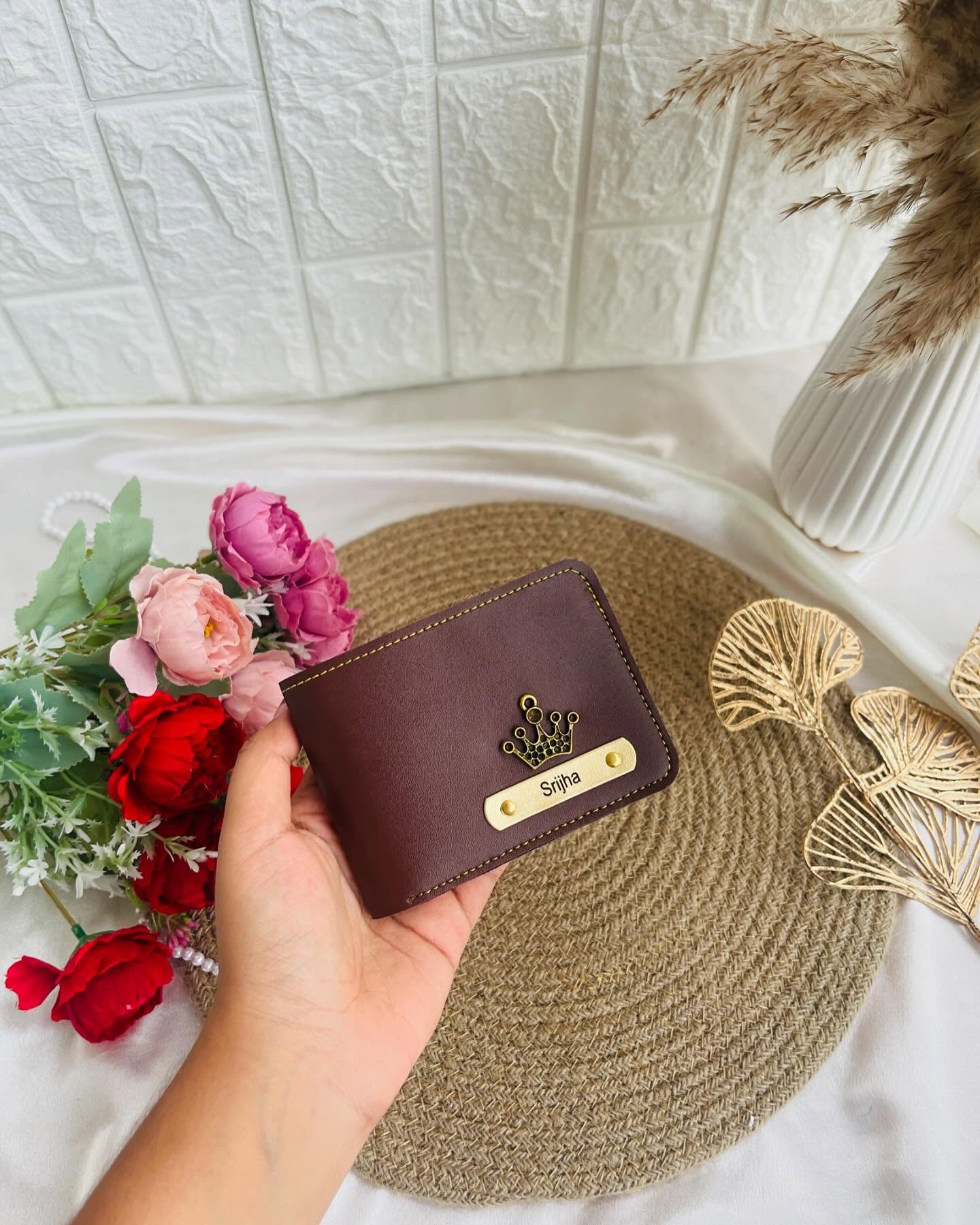 A handcrafted burgundy leather wallet with a custom name plate and gold crown charm.