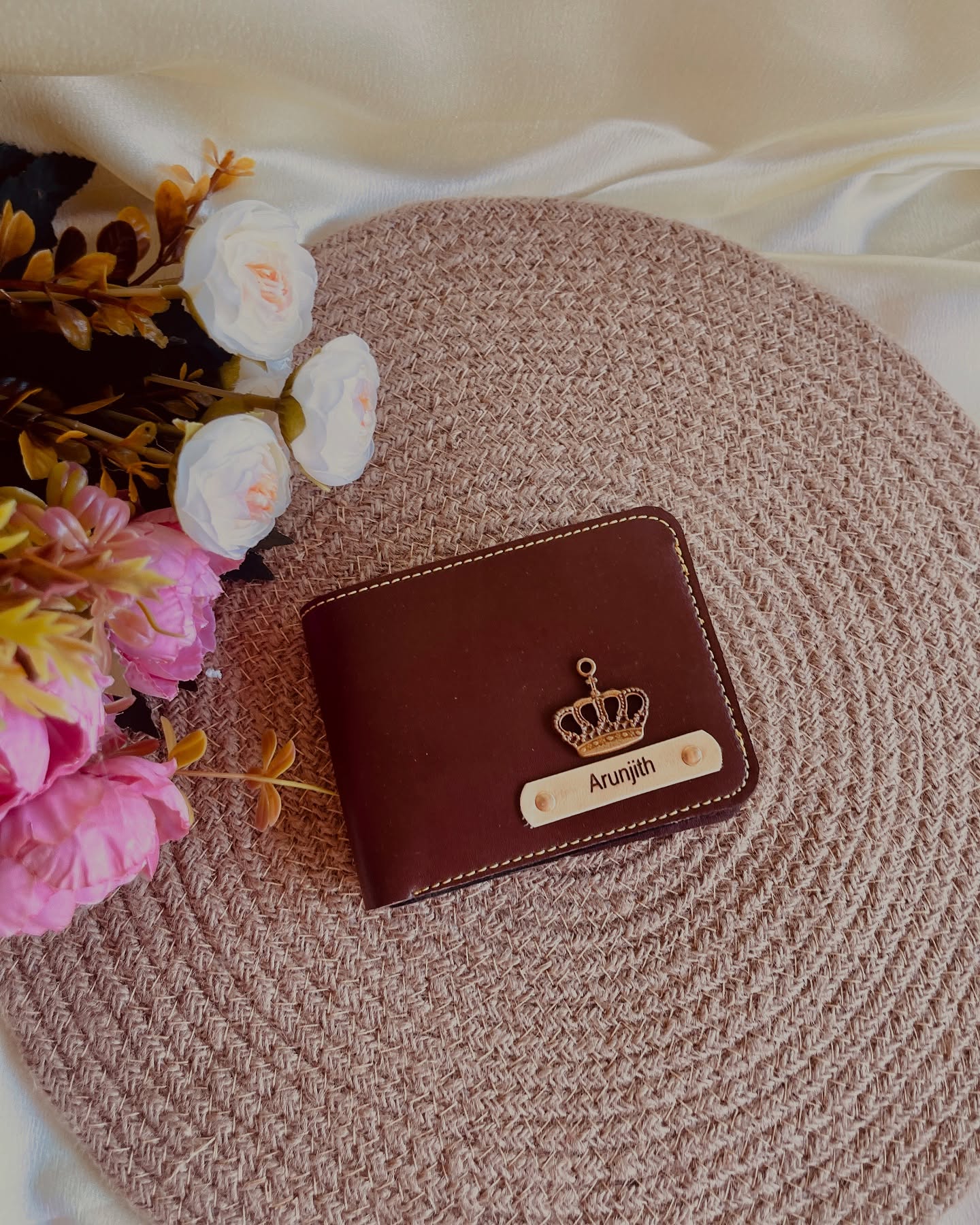 A rich brown leather bifold wallet embossed with a gold crown charm and a custom engraved name tag.