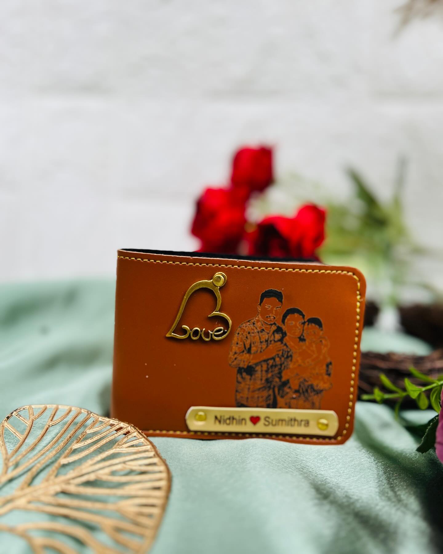 A tan leather bifold wallet engraved with a couple's family portrait and their names on a brass nameplate.