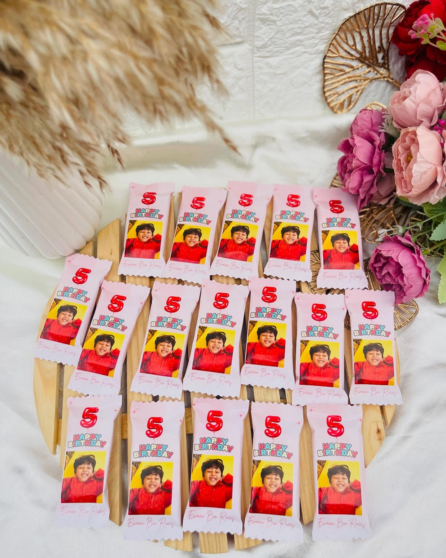 A large batch of custom chocolate bars printed with a child's photo, name and birthday age balloon design.
