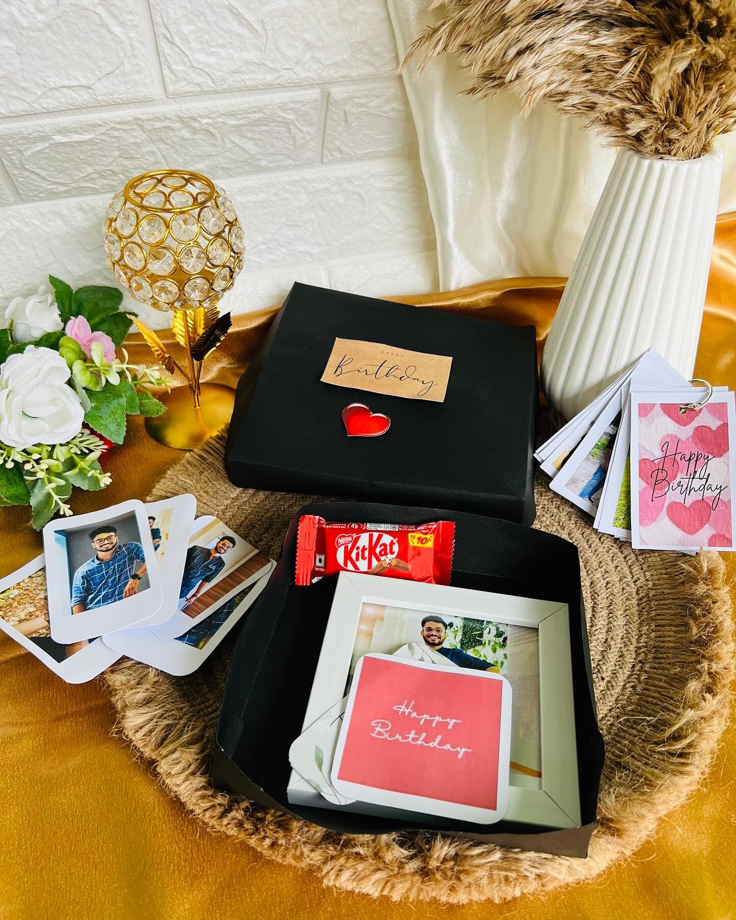 A black birthday gift box with a personalized photo frame, KitKat, custom cards, and a stack of polaroid prints.