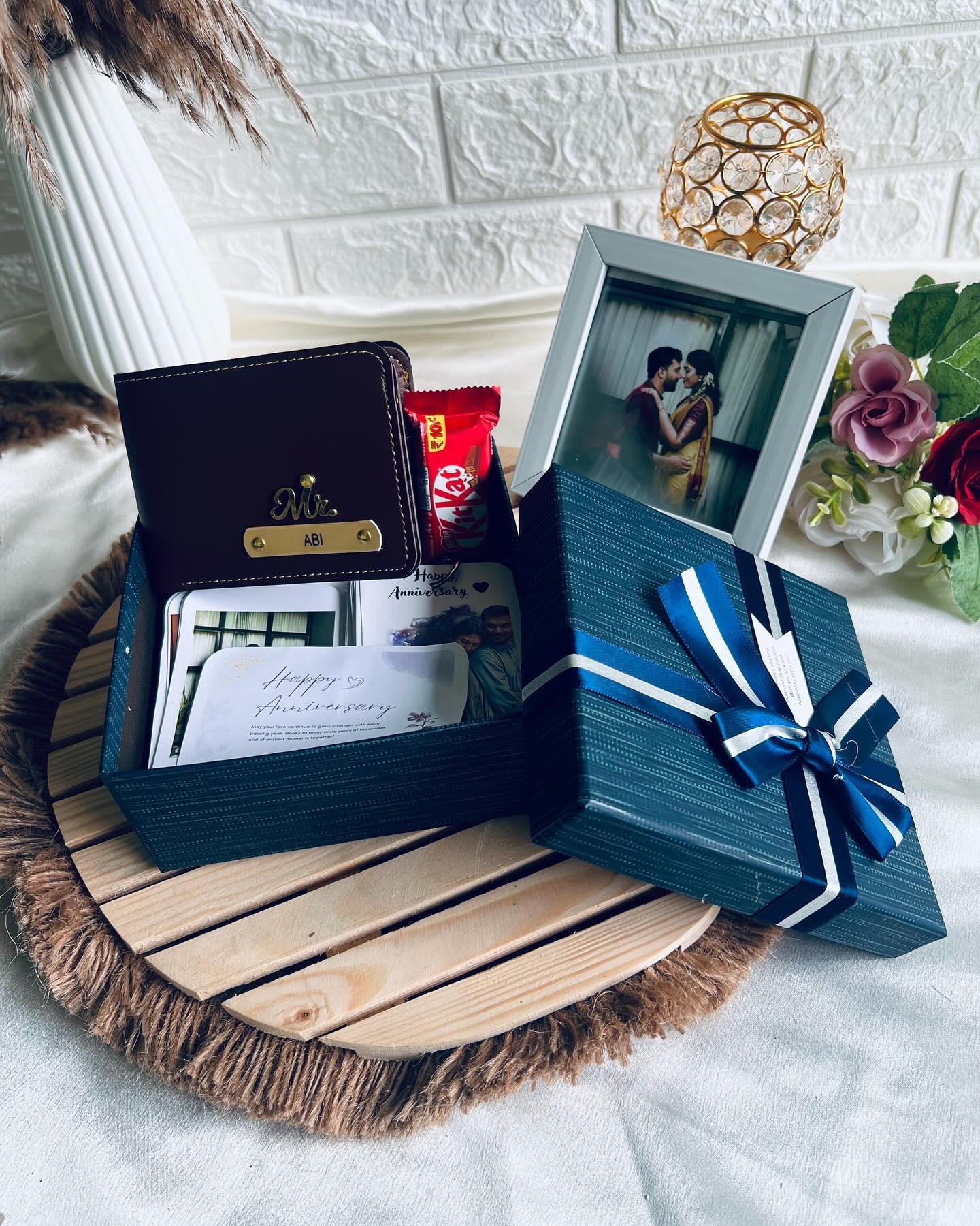 A monogrammed leather wallet paired with mini polaroid keepsakes and chocolate in a ribboned anniversary gift box.