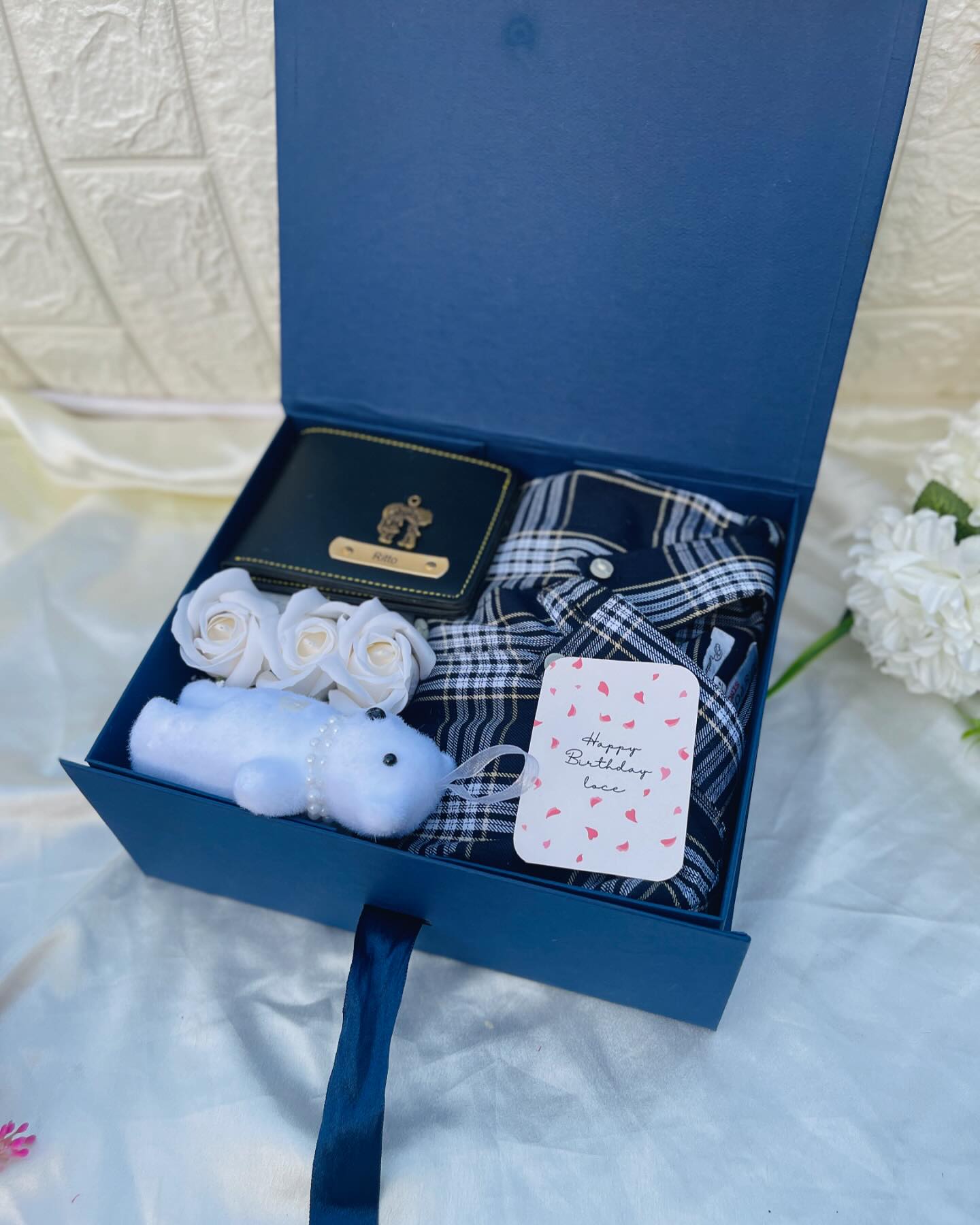 A navy birthday gift box with a name-engraved wallet, checked flannel shirt, plush charm, and roses.