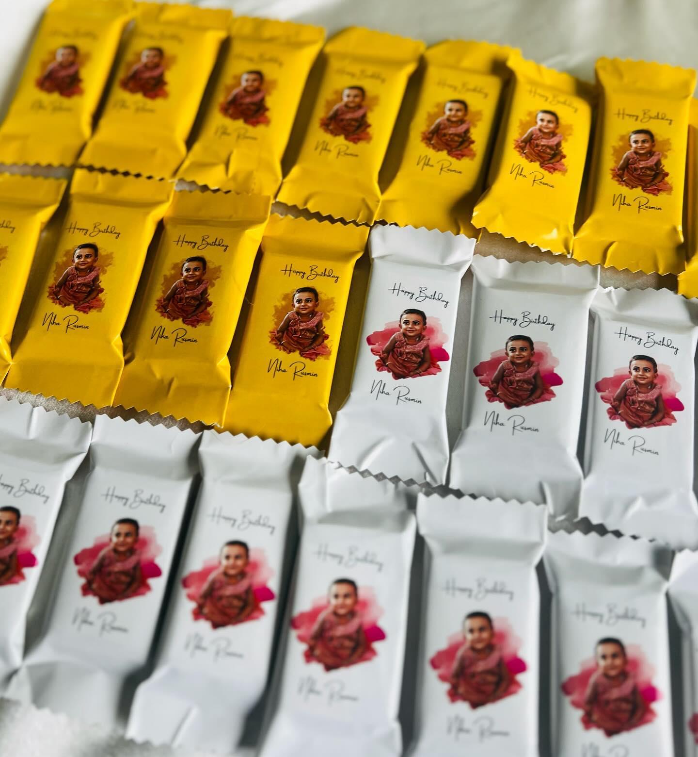A stack of individually wrapped chocolate bars printed with the birthday child's photo and name, perfect as party favors.