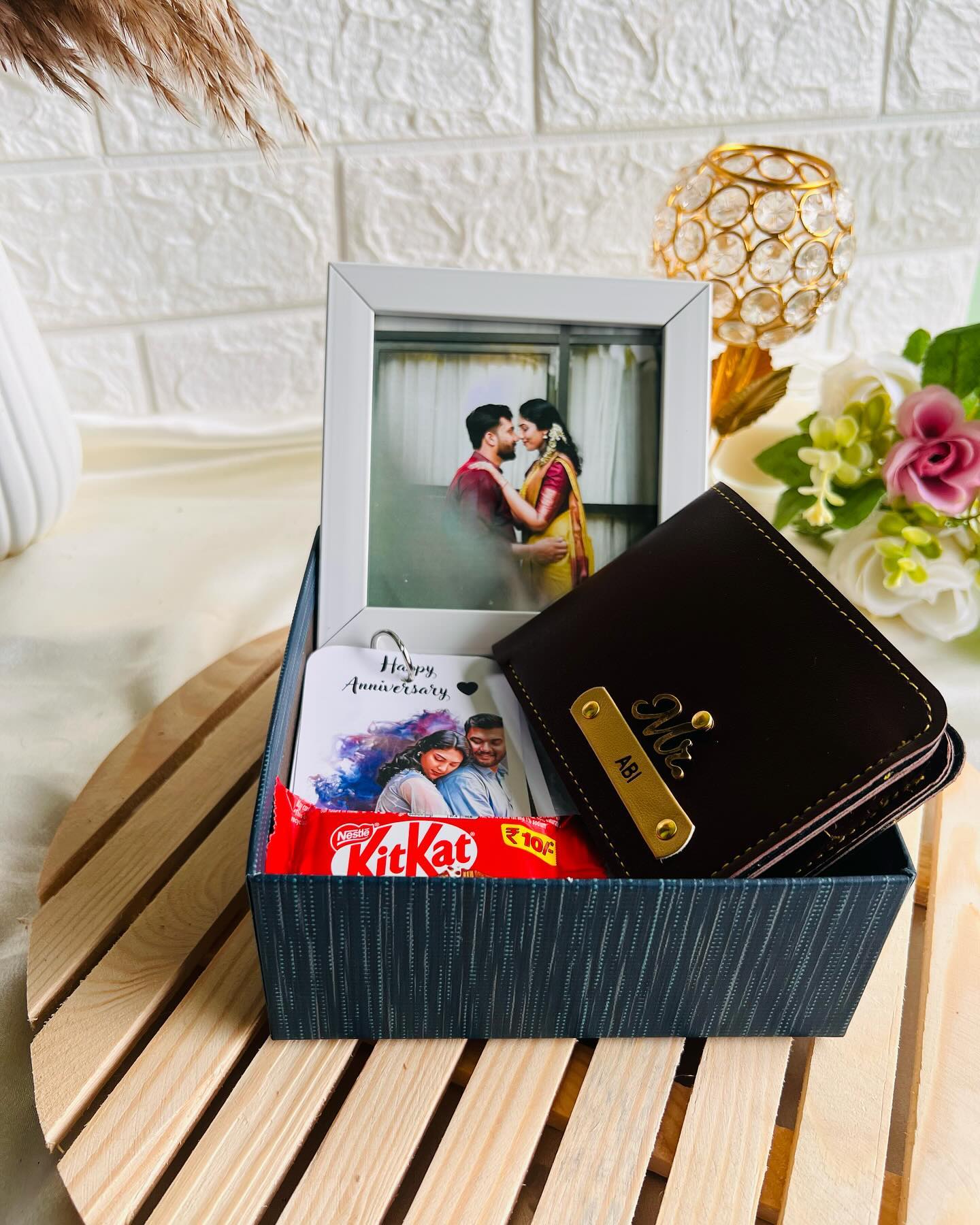 An anniversary gift box featuring a couple photo frame, a name-personalized leather wallet, a keepsake card, and KitKat.