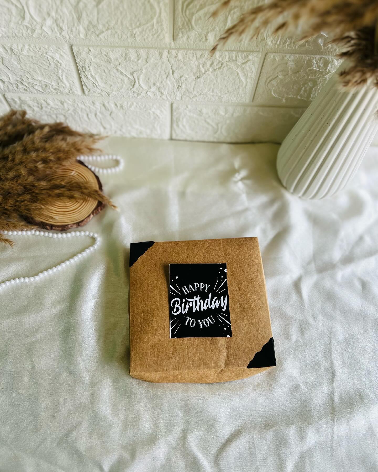A rustic kraft birthday box filled with printed photo cards, a KitKat treat, and a handwritten birthday note.