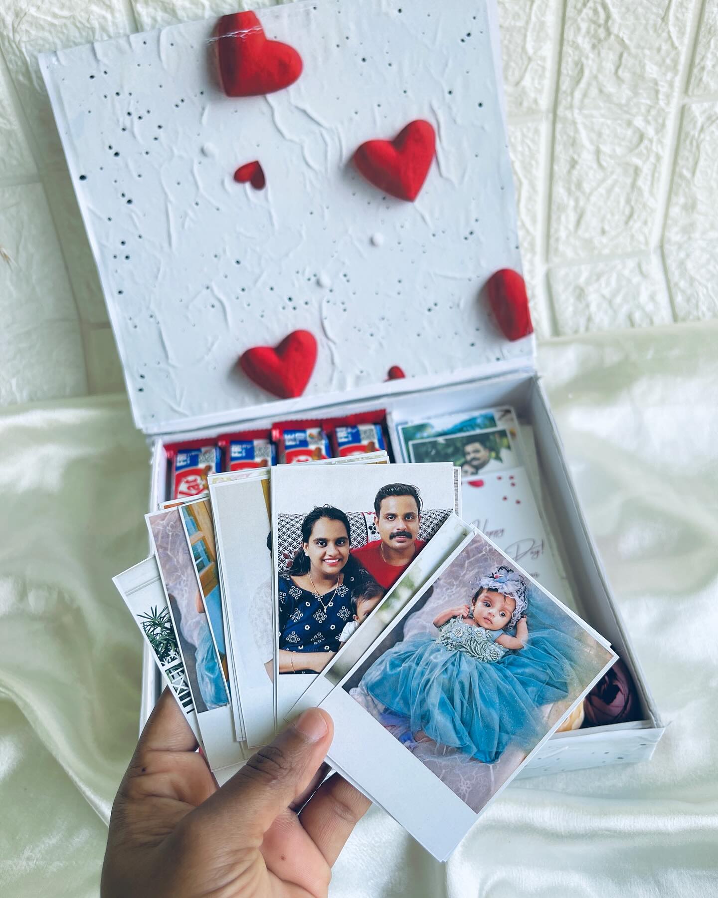 A heart-embossed keepsake box filled with printed family photos and KitKat chocolates.