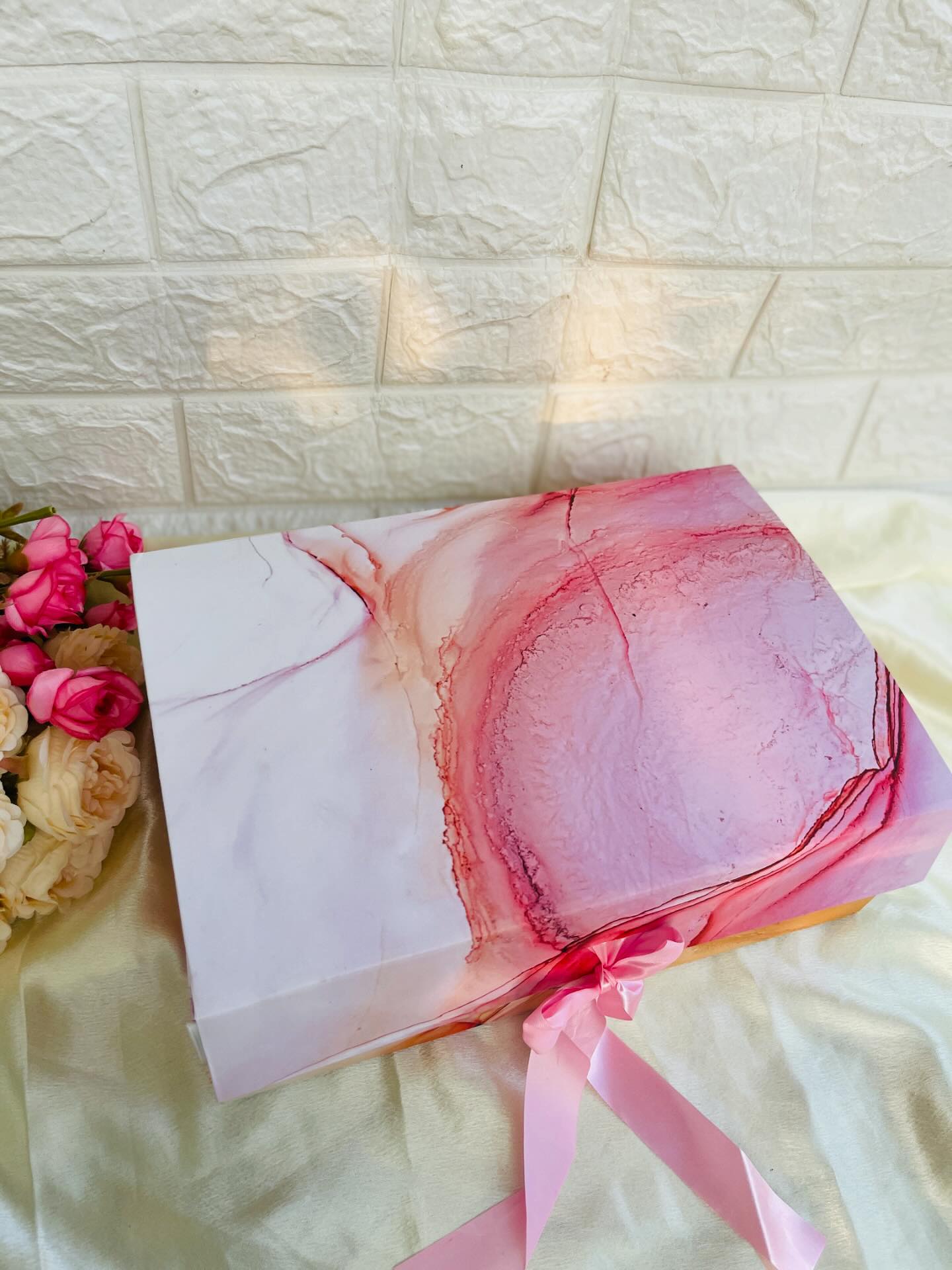 A pink and white marble-patterned gift box tied with a satin pink ribbon, styled with fresh roses.