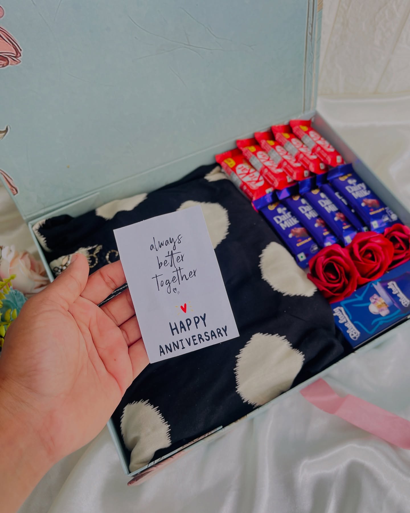 A duck-egg blue anniversary box with a polka-dot scarf, KitKat and Dairy Milk bars, red roses, and a handwritten card.