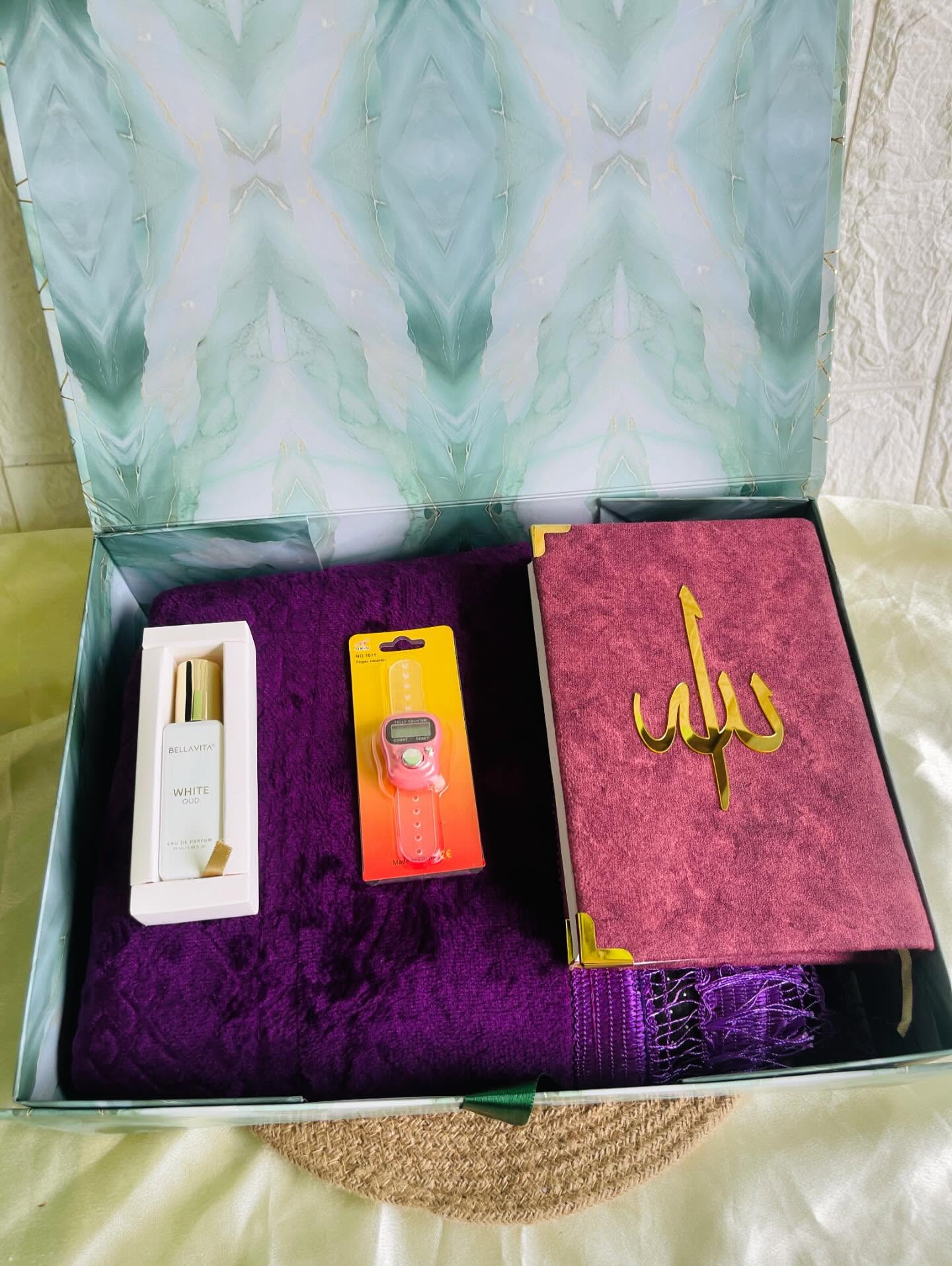 A mint keepsake box with a plush purple prayer mat, a velvet-bound Islamic prayer book, Bellavita White Oud perfume and a tasbeeh counter.