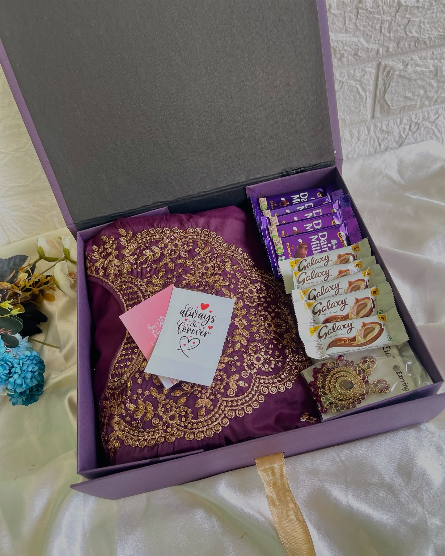 A regal purple embroidered saree paired with Cadbury and Galaxy chocolates, statement earrings, and a heartfelt birthday card.