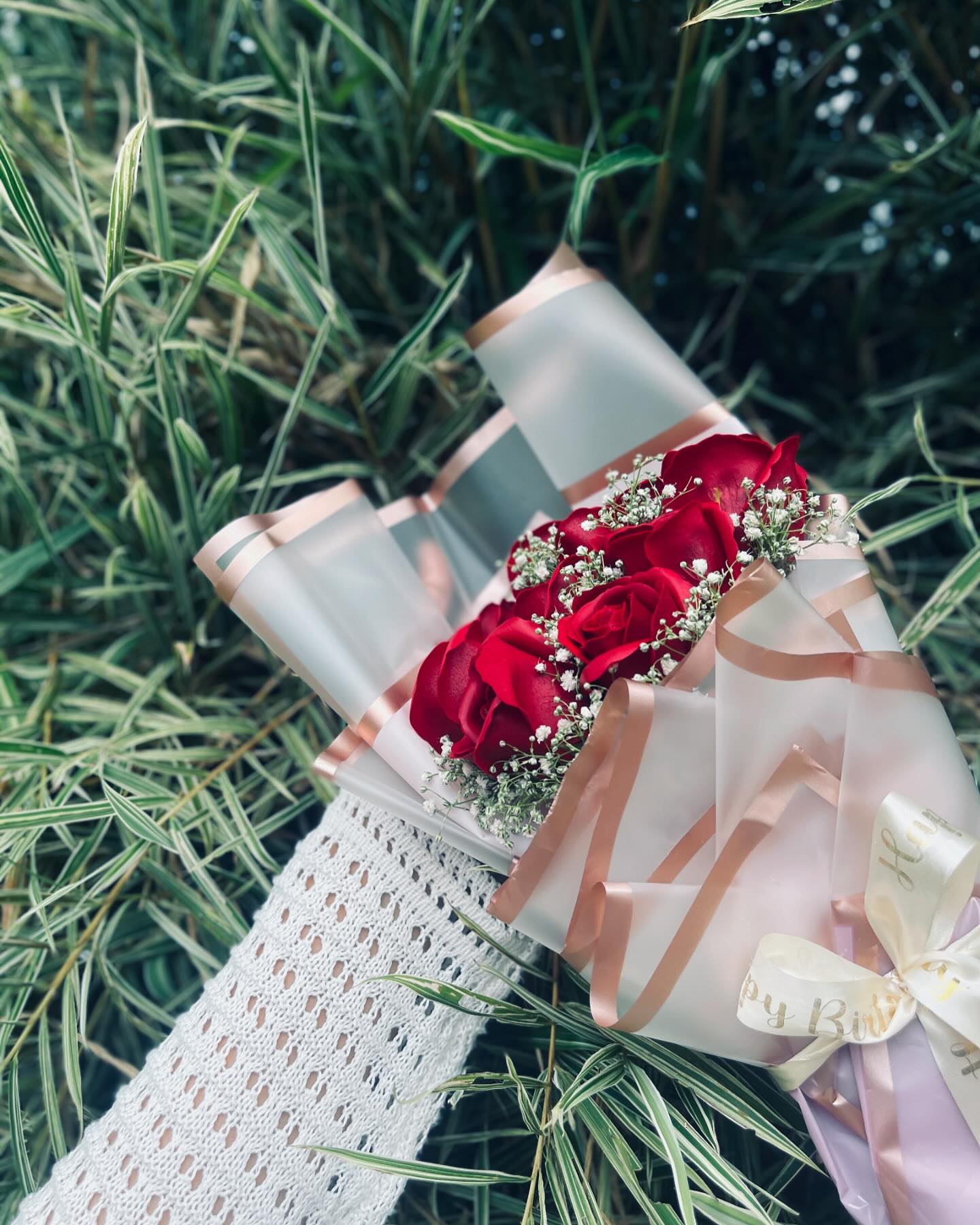 A romantic bouquet of red roses and baby's breath wrapped in rose-gold trimmed paper with a "Happy Birthday" ribbon.