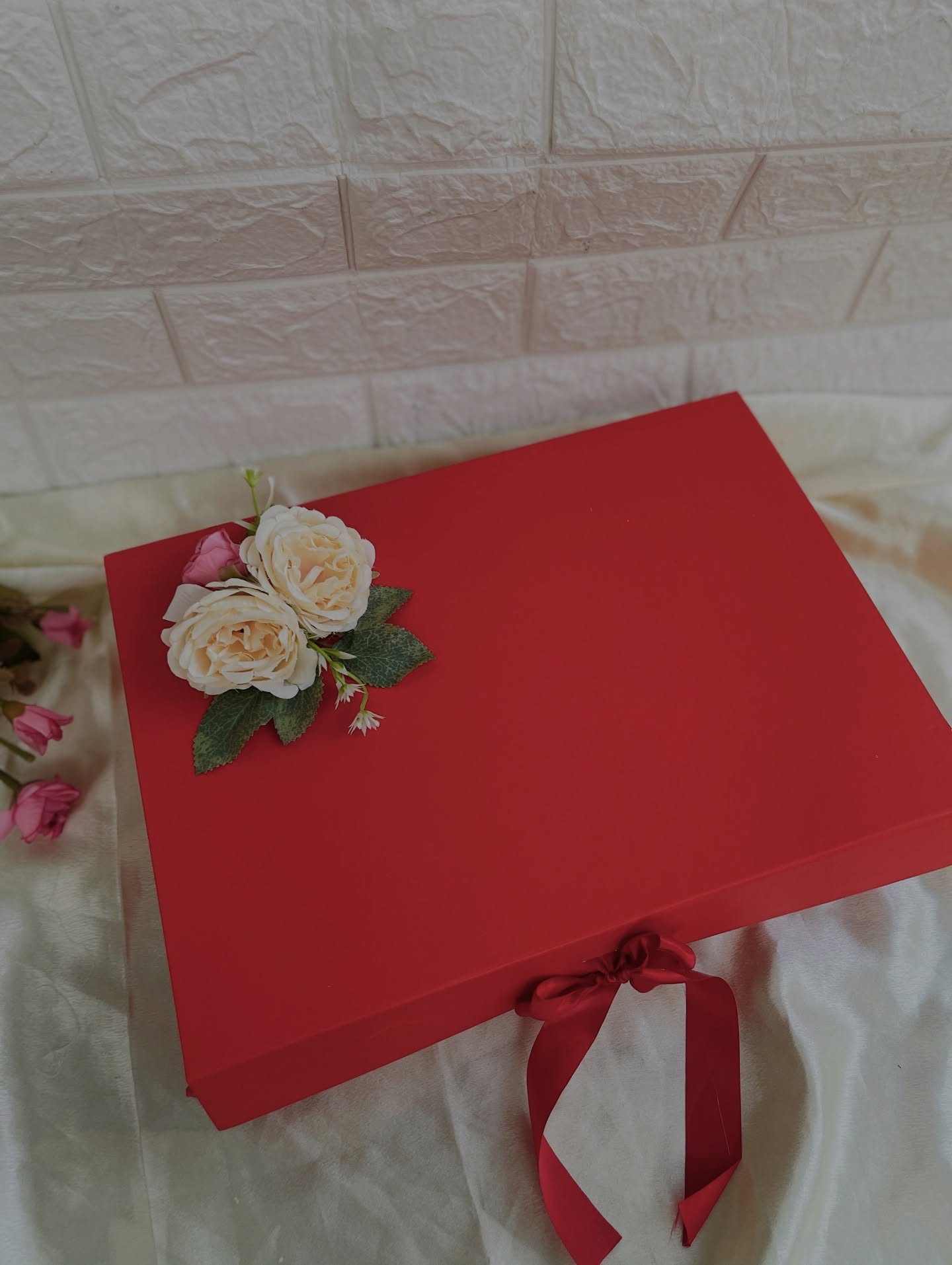 A bold red gift box tied with a satin ribbon and topped with a small rose corsage.