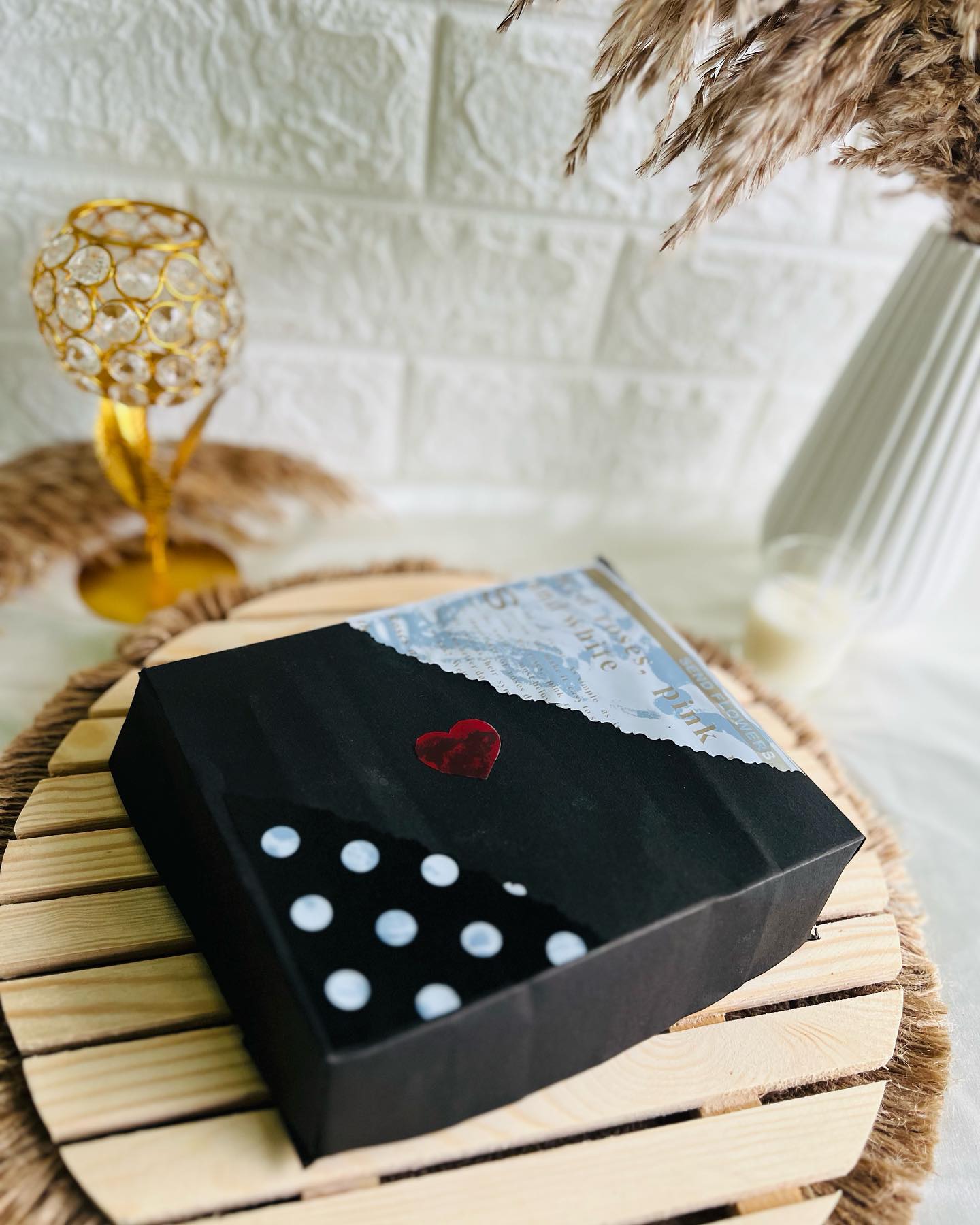 An elegant black gift box wrapped in a rose-print design and finished with a red heart accent.