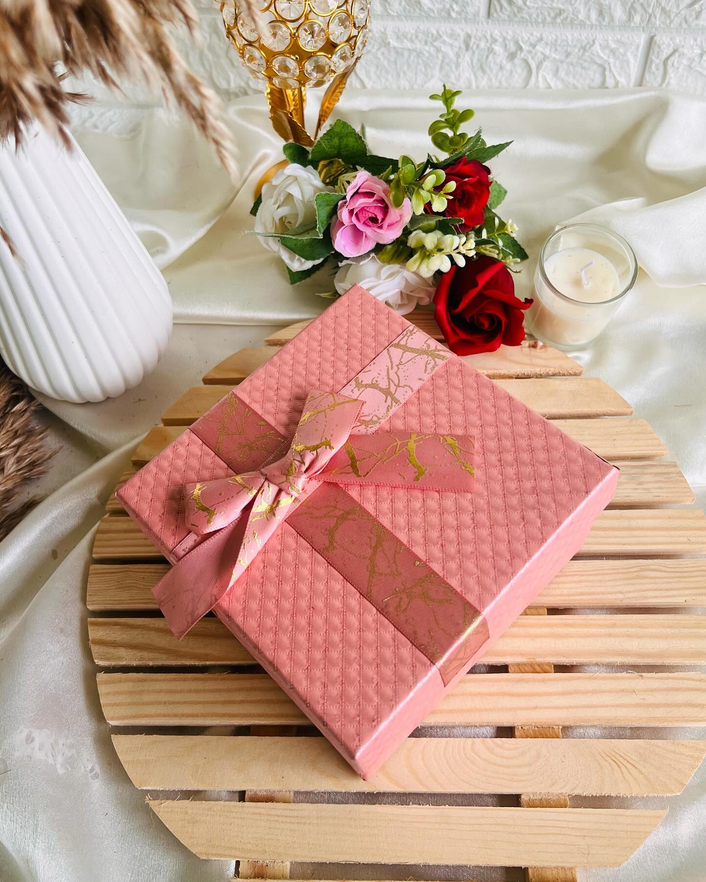 A pink gift box filled with red roses, KitKat chocolate, and a personalized polaroid photo print.