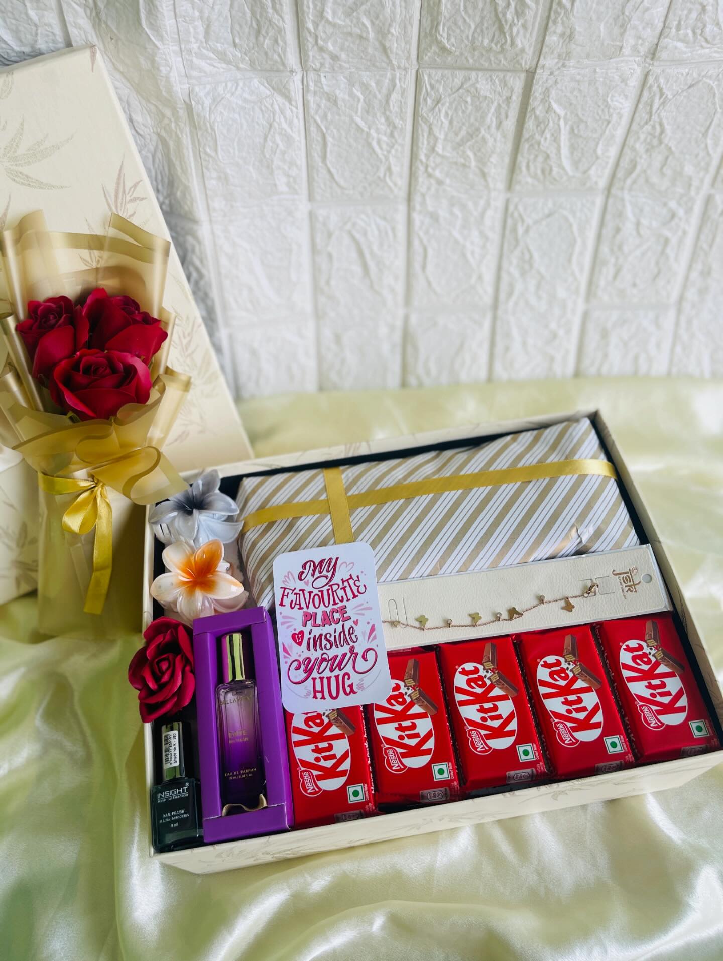 A cream gift box loaded with a red rose bouquet, perfume, nail polish and a stack of KitKat bars with a romantic note.