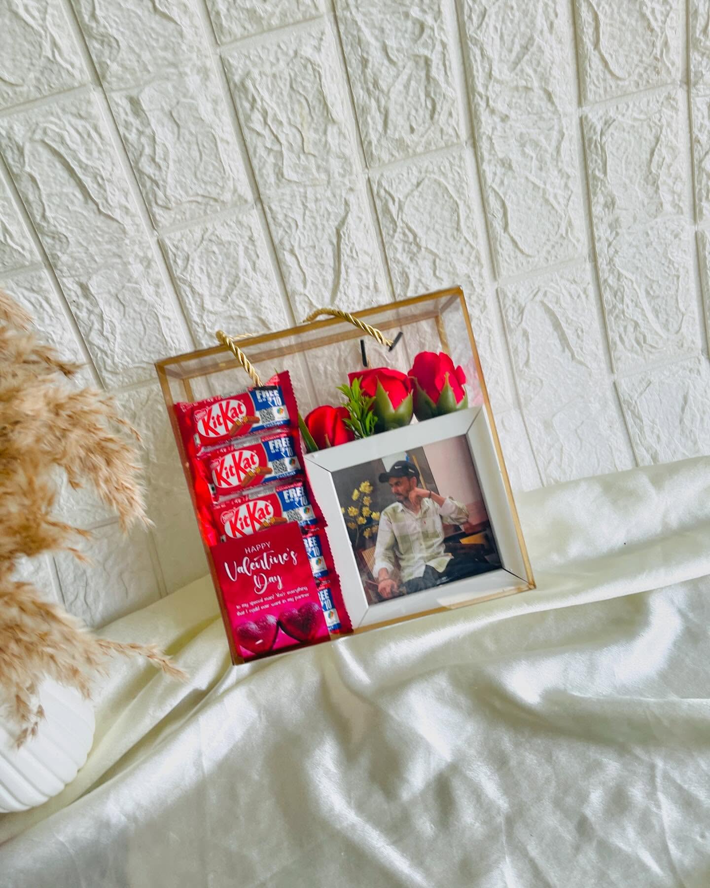 A mirrored keepsake frame holding a couple's photo, red roses, and a row of KitKat bars for Valentine's Day.